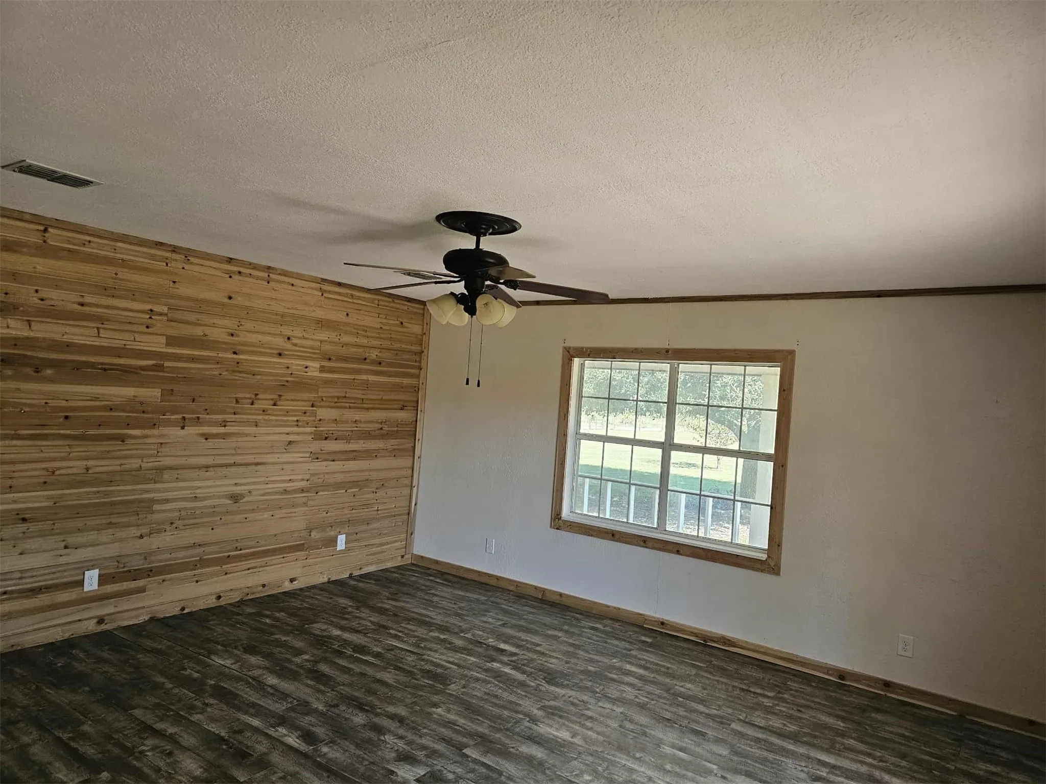 Spare room with wood walls, dark wood-type flooring, a textured ceiling, and a ceiling fan