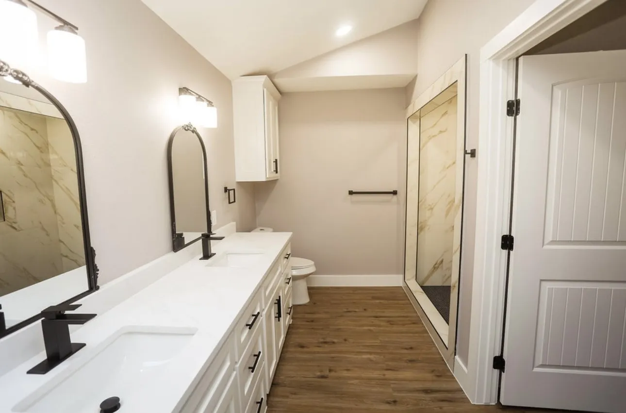 Full bathroom featuring dark wood-style flooring, double vanity, lofted ceiling, a marble finish shower, and recessed lighting