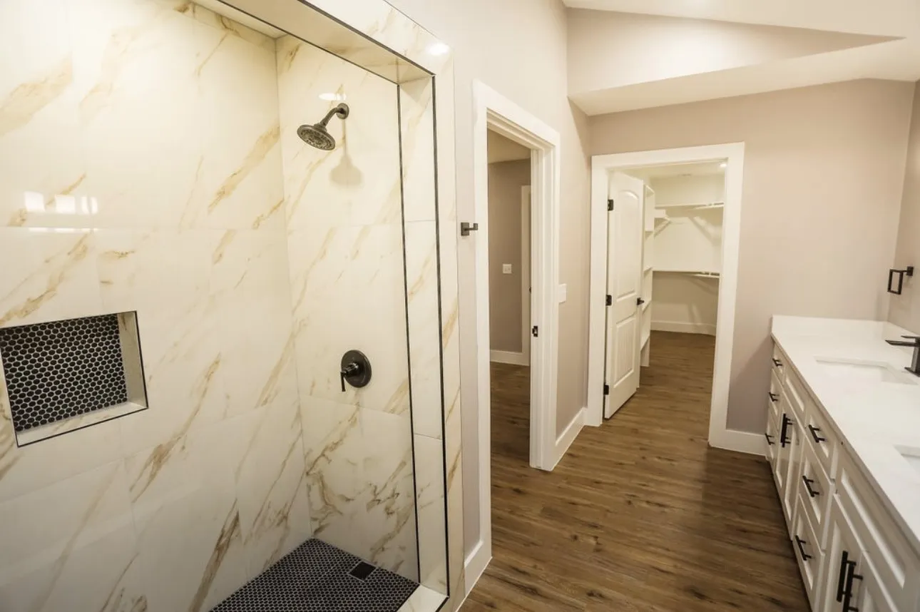 Bathroom featuring a marble finish shower, double vanity, a spacious closet, and dark wood-style floors