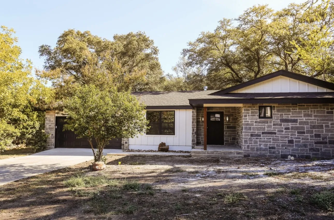 View of front of property featuring board and batten siding, driveway, stone siding, and covered porch