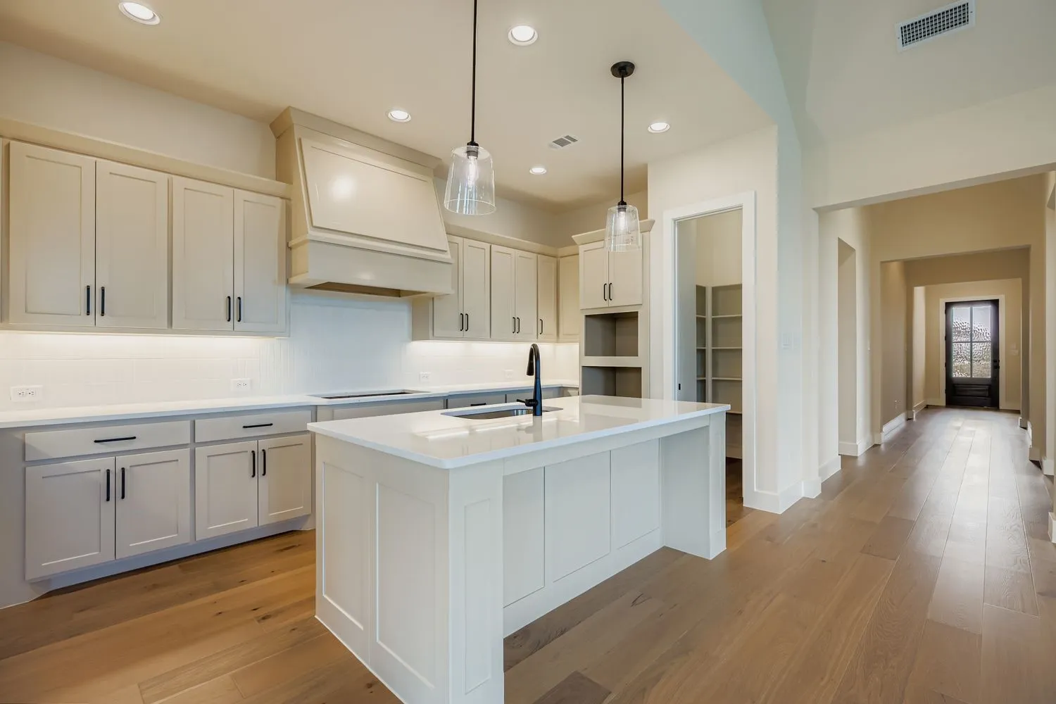 Kitchen featuring decorative light fixtures, decorative backsplash, light stone countertops, an island with sink, and light wood-style floors