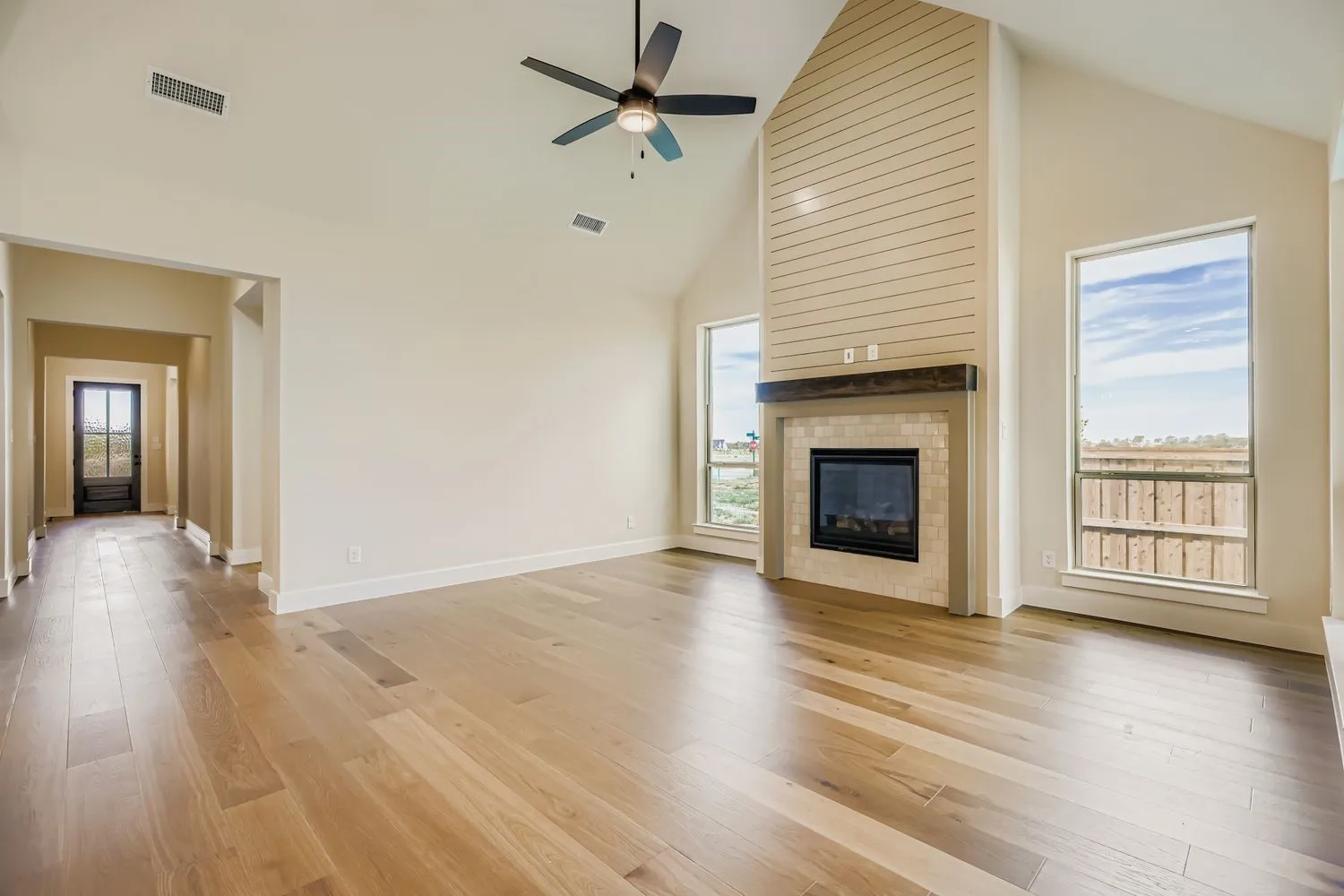 Unfurnished living room featuring high vaulted ceiling, light wood-type flooring, a fireplace, and a ceiling fan