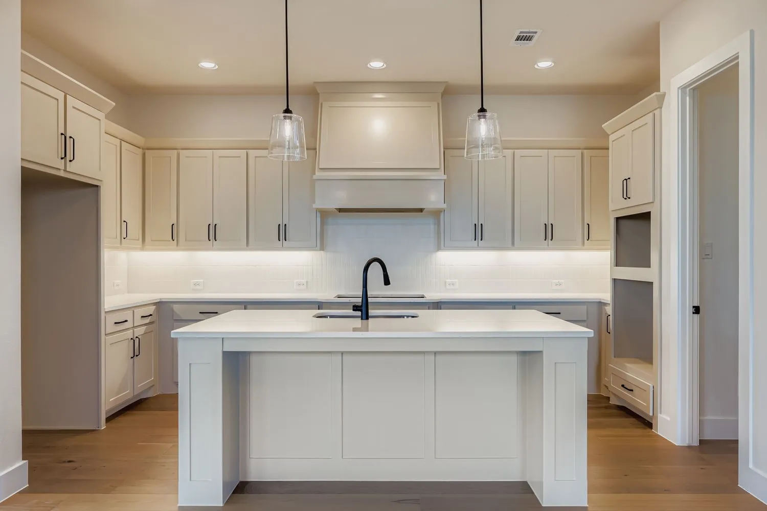 Kitchen with hanging light fixtures, recessed lighting, a center island with sink, light stone countertops, and wood finished floors