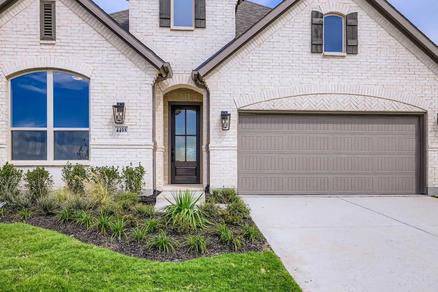 French country home featuring an attached garage, concrete driveway, brick siding, and roof with shingles