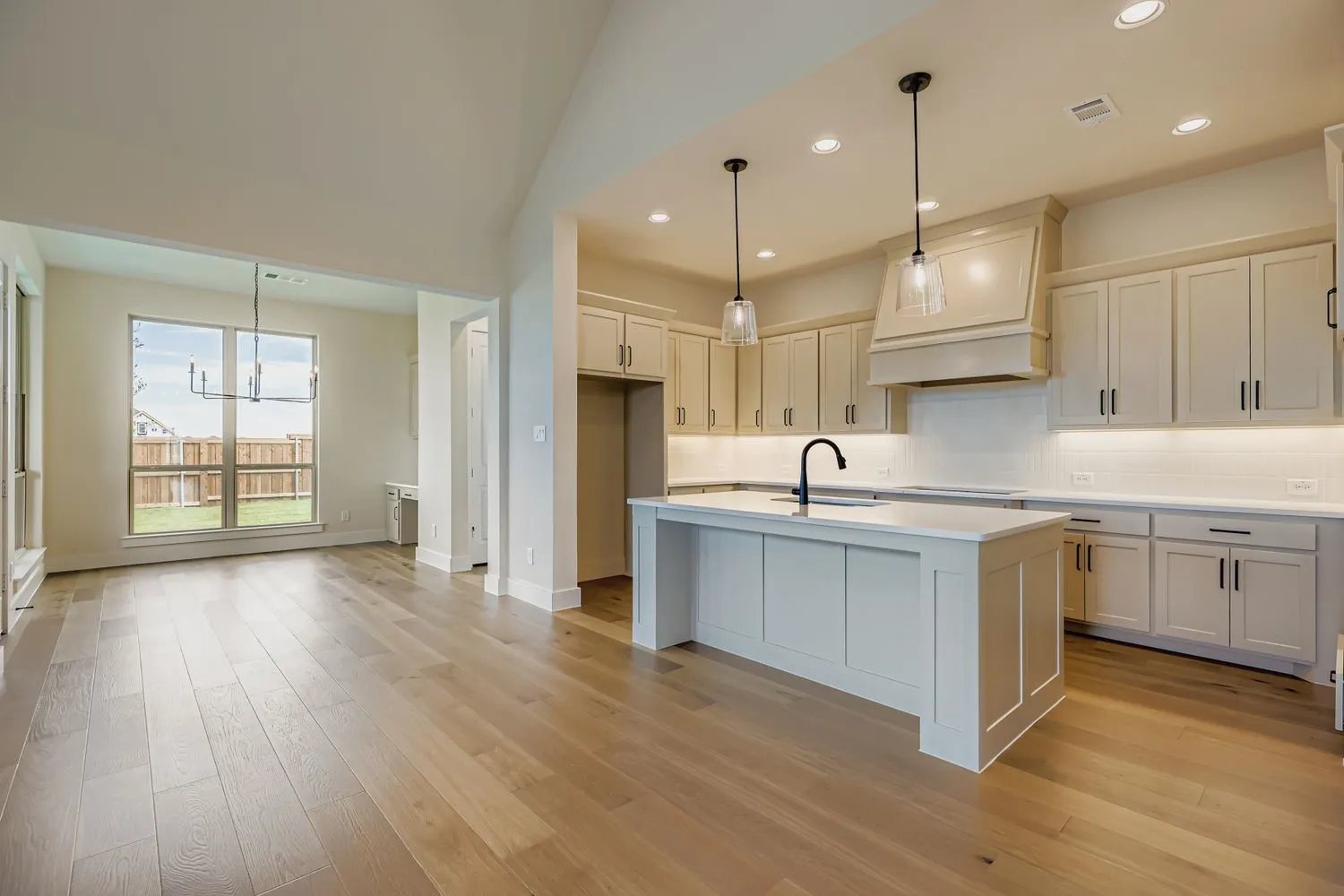 Kitchen with tasteful backsplash, hanging light fixtures, a kitchen island with sink, light wood finished floors, and a kitchen breakfast bar
