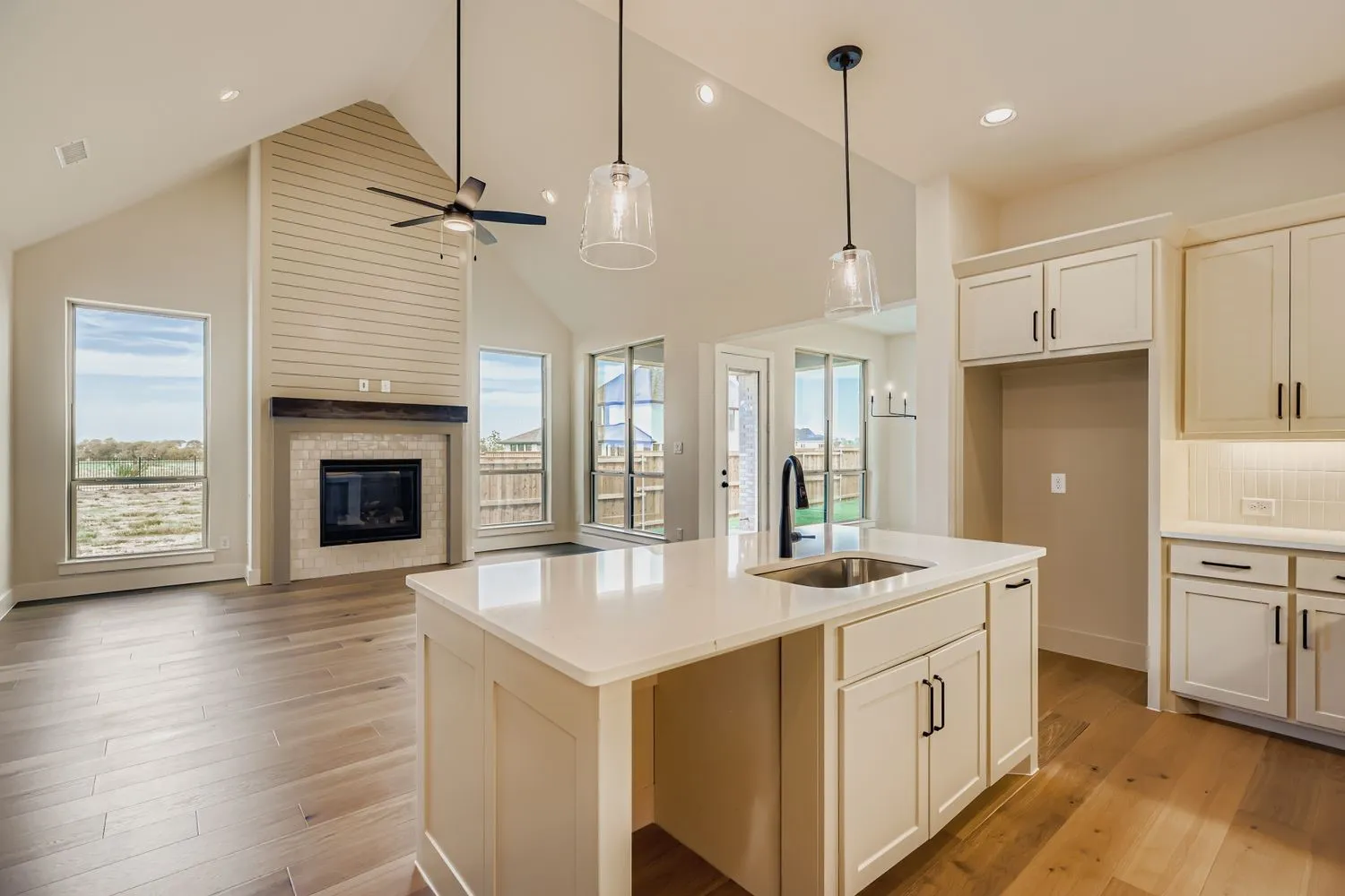 Kitchen with high vaulted ceiling, hanging light fixtures, light wood-type flooring, open floor plan, and a center island with sink