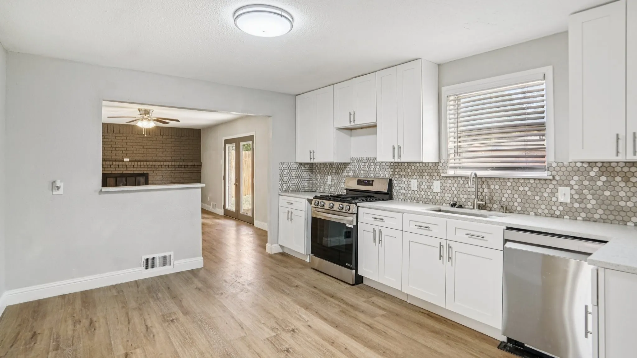 Kitchen with white cabinetry, appliances with stainless steel finishes, backsplash, light wood-type flooring, and a brick fireplace