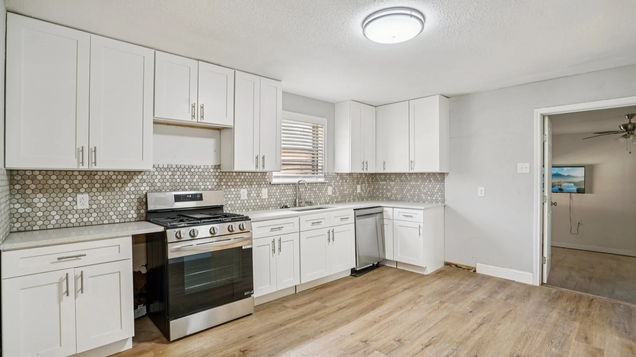 Kitchen with white cabinetry, appliances with stainless steel finishes, light wood-style floors, backsplash, and a textured ceiling