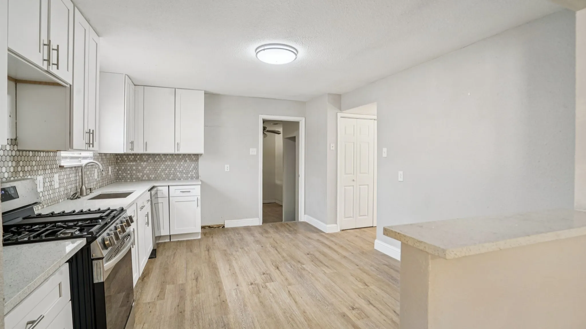 Kitchen with gas range, tasteful backsplash, light stone counters, light wood-style floors, and white cabinets