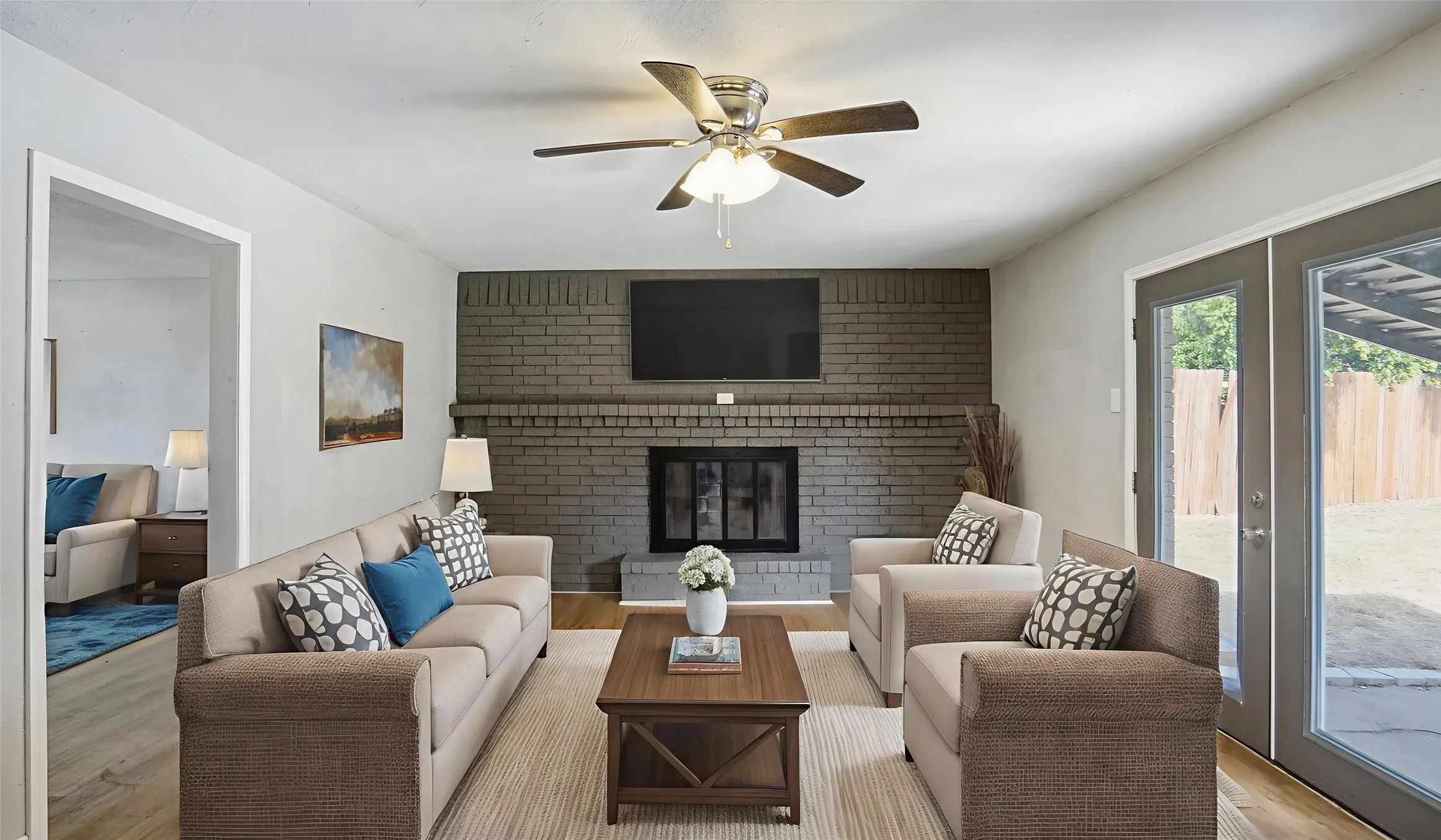 Living area featuring a brick fireplace, wood finished floors, a ceiling fan, and french doors. Virtual Staged