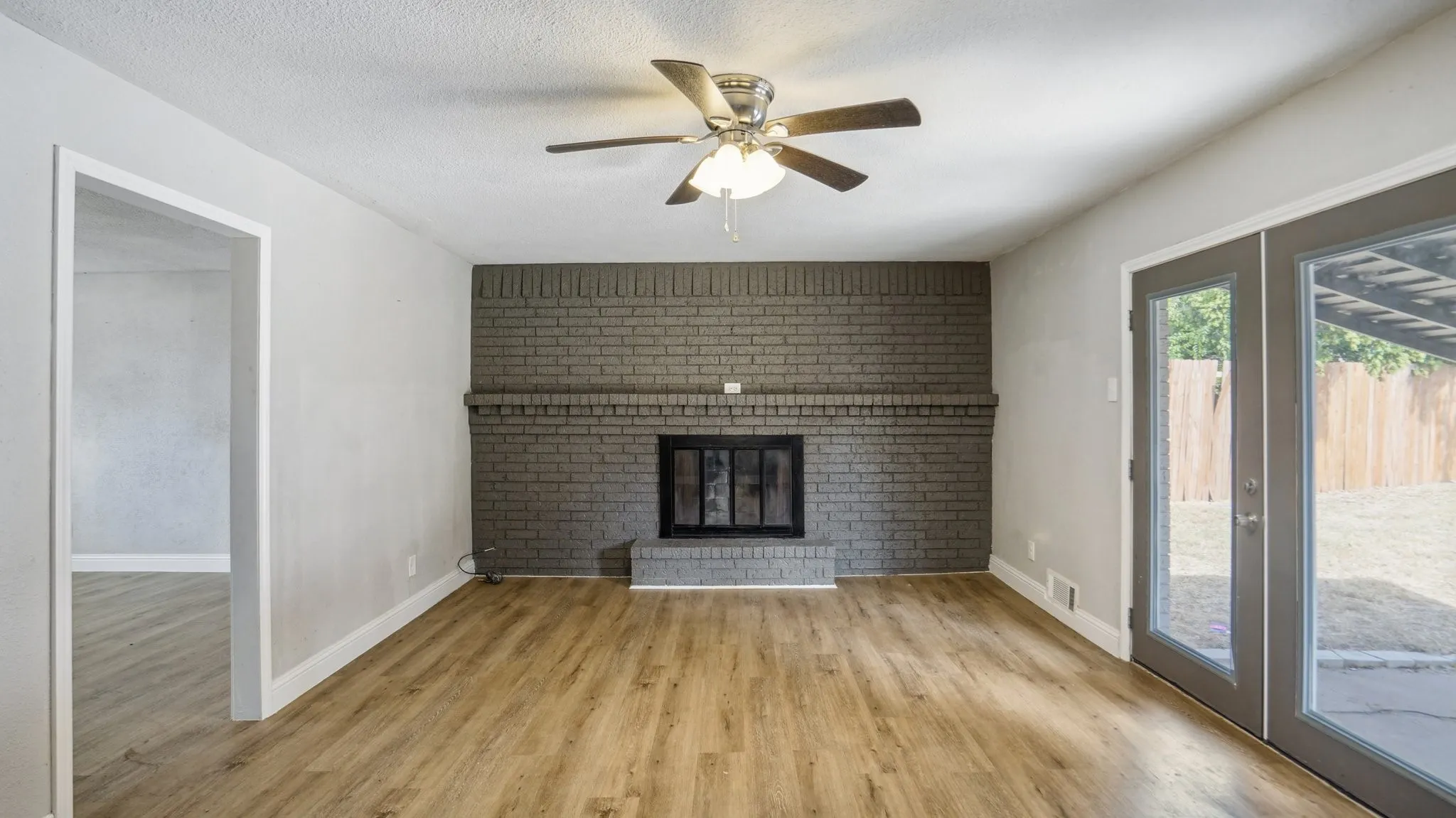 Unfurnished living room with light wood finished floors, a fireplace, a ceiling fan, brick wall, and a textured ceiling