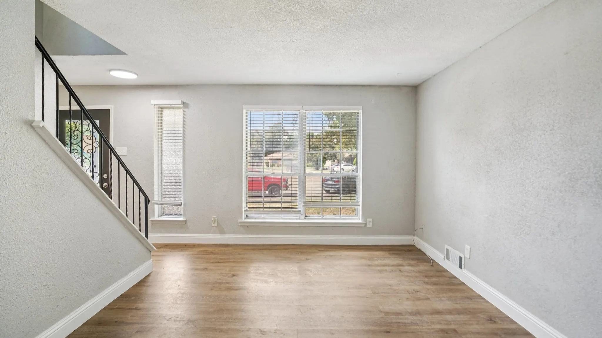 Unfurnished living room with a textured wall, stairway, light wood finished floors, and a textured ceiling