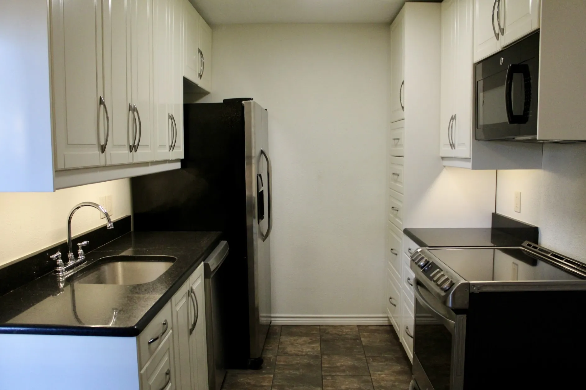 Kitchen featuring stainless steel appliances, white cabinets, dark stone counters, and stone finish flooring