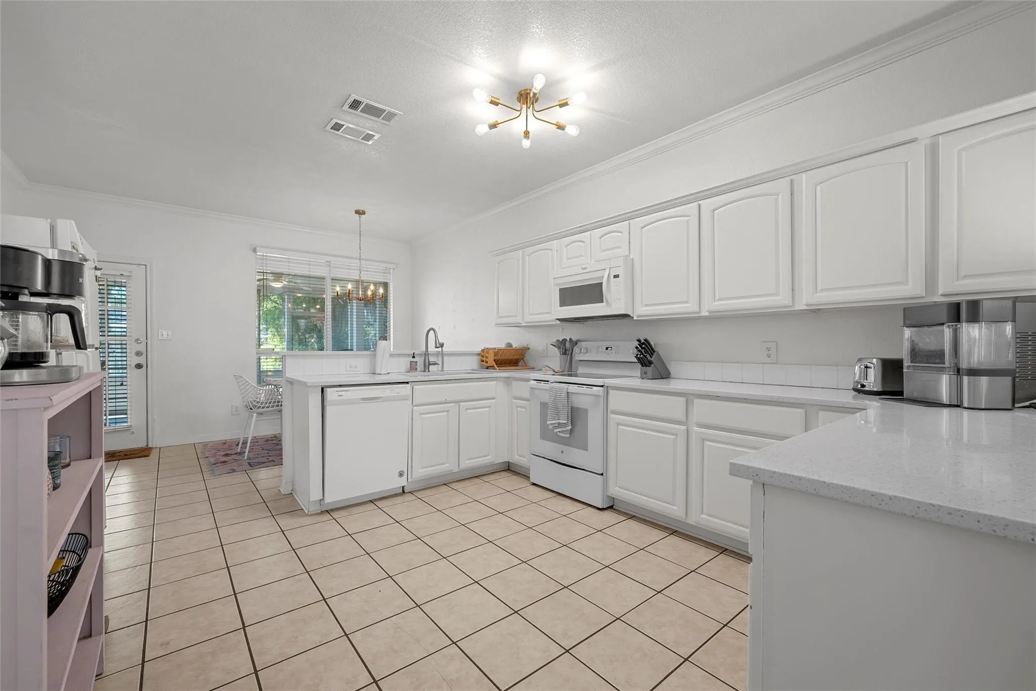 Kitchen featuring a chandelier, a peninsula, ornamental molding, white appliances, and white cabinetry