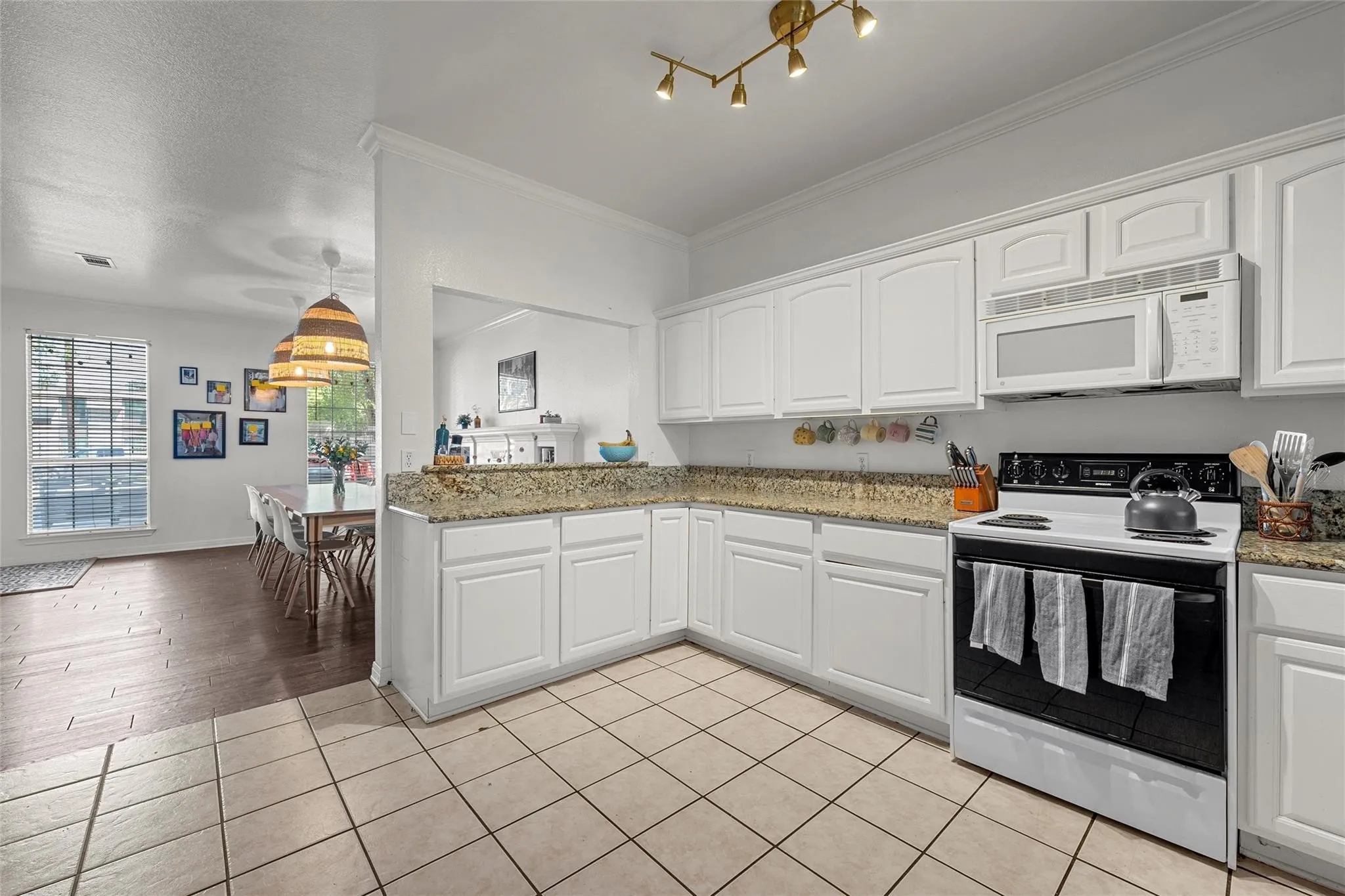 Kitchen with white appliances, white cabinets, light stone countertops, light tile patterned flooring, and ornamental molding