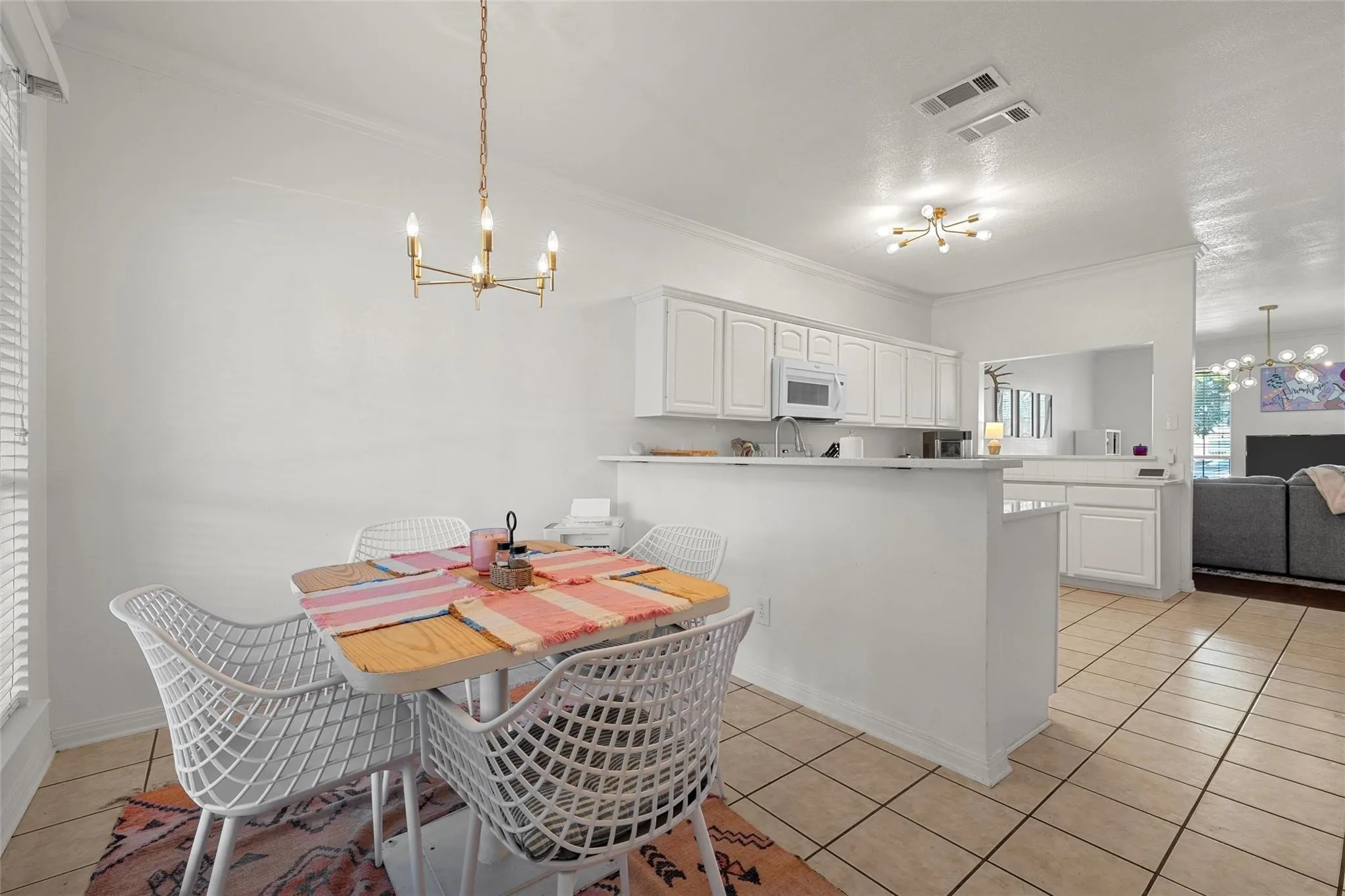 Kitchen featuring a chandelier, pendant lighting, a peninsula, white cabinetry, and ornamental molding