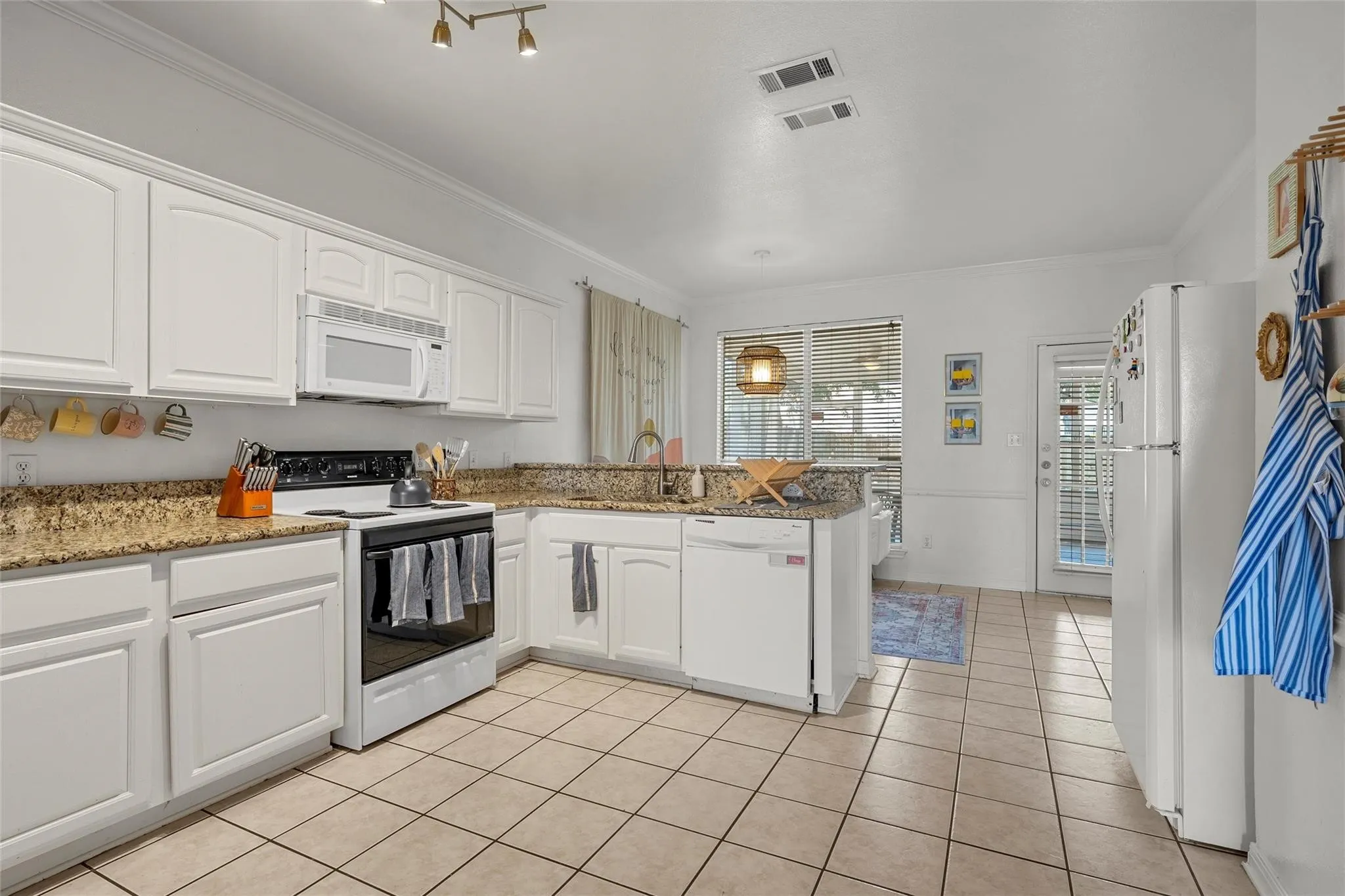 Kitchen featuring white appliances, white cabinets, a peninsula, light stone counters, and ornamental molding