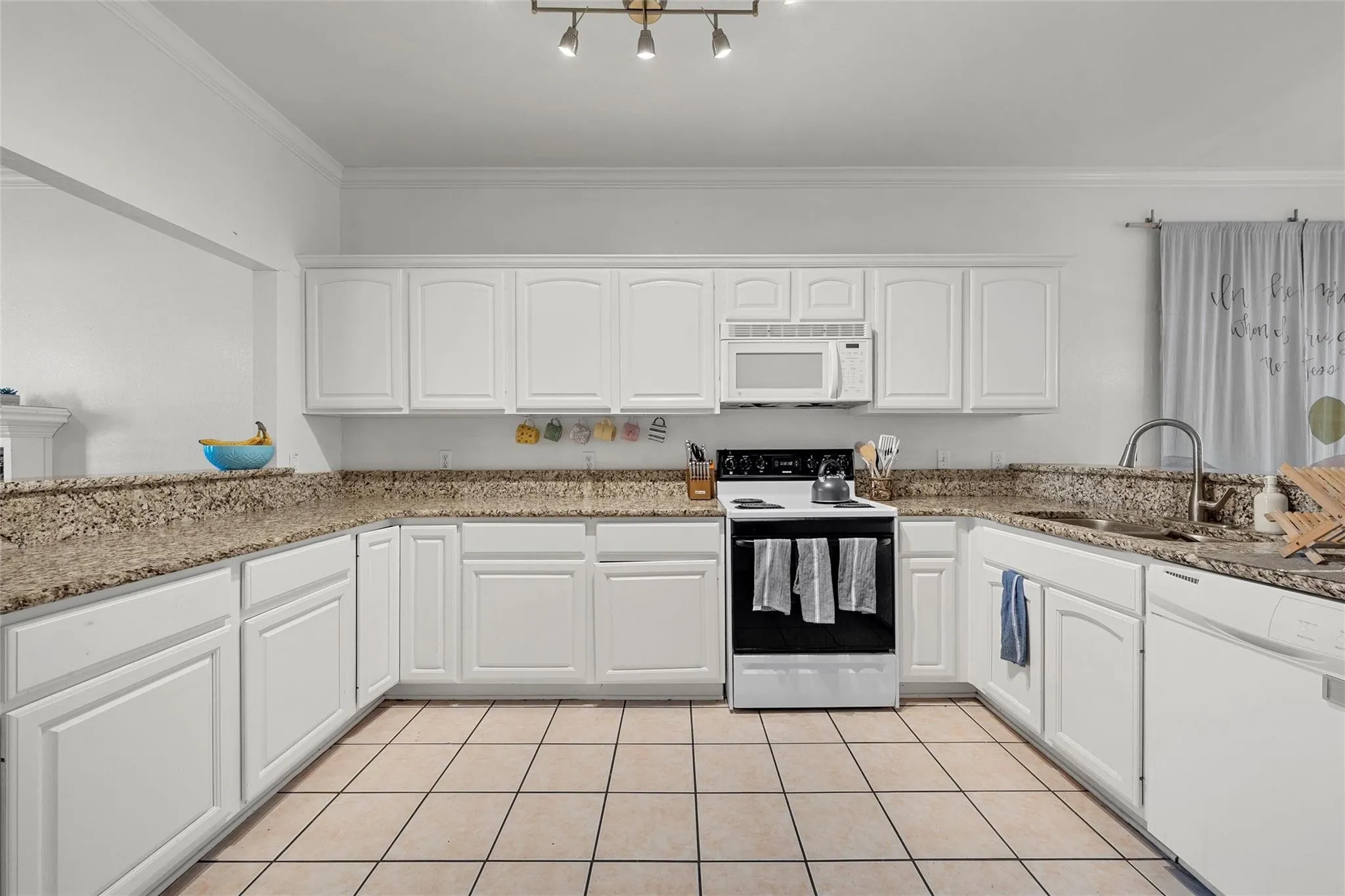 Kitchen with white appliances, white cabinetry, light tile patterned flooring, crown molding, and light stone countertops