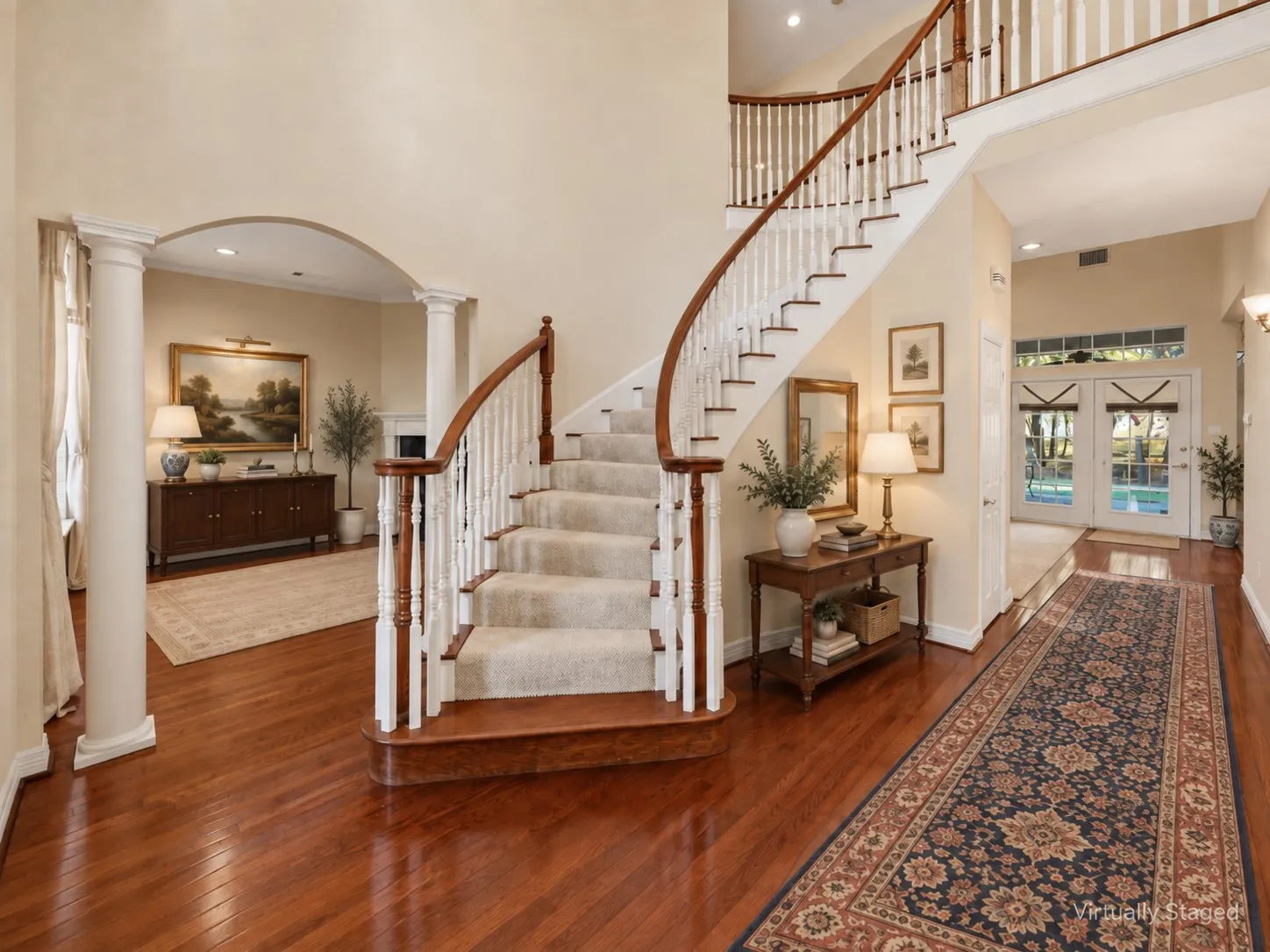 Grand foyer with a curved staircase, wood-finish flooring, white balusters, and a double-door entry