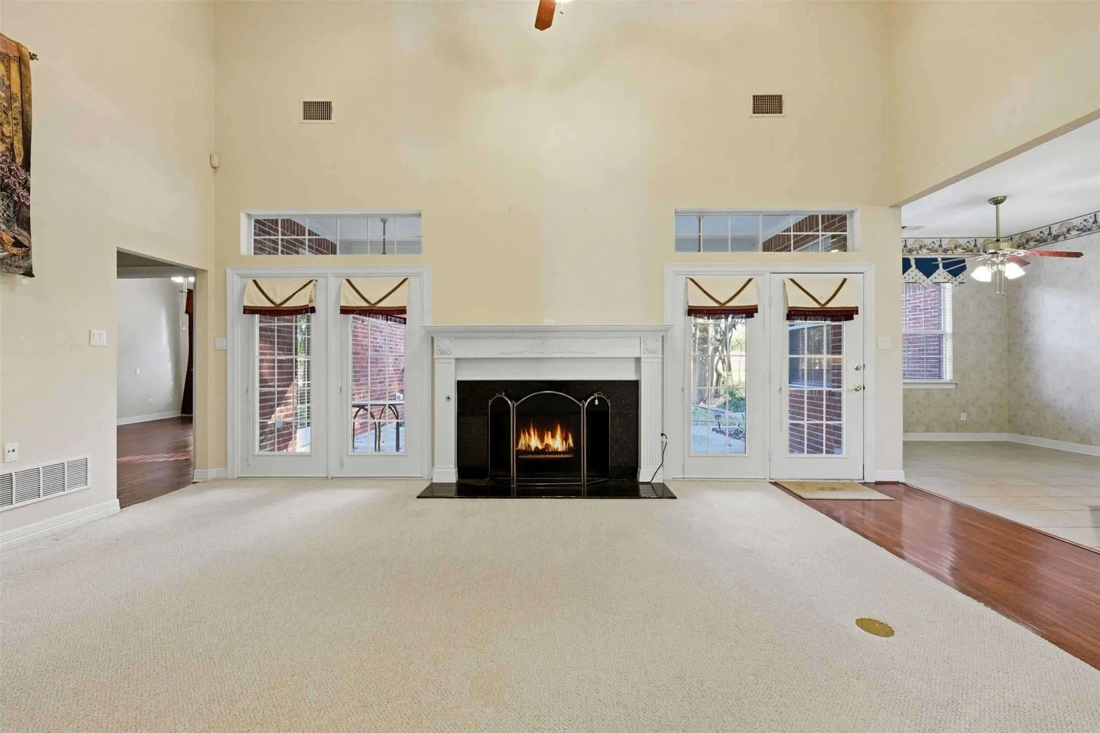 living room featuring ceiling fan, carpet floors, a fireplace, wood finished floors, and a towering ceiling