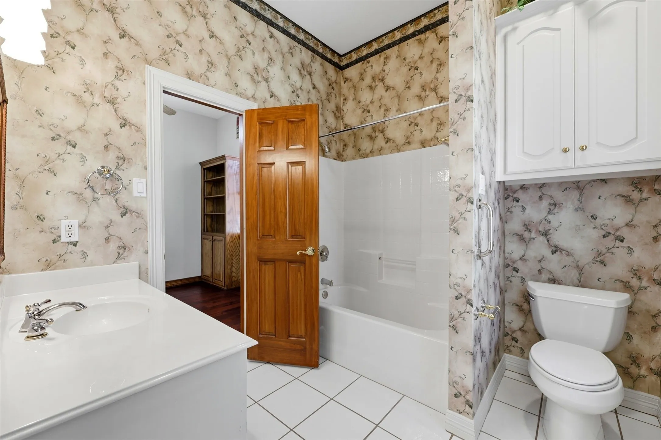 1st floor Full bath with wallpapered walls, vanity, light tile patterned floors, and shower / bath combo