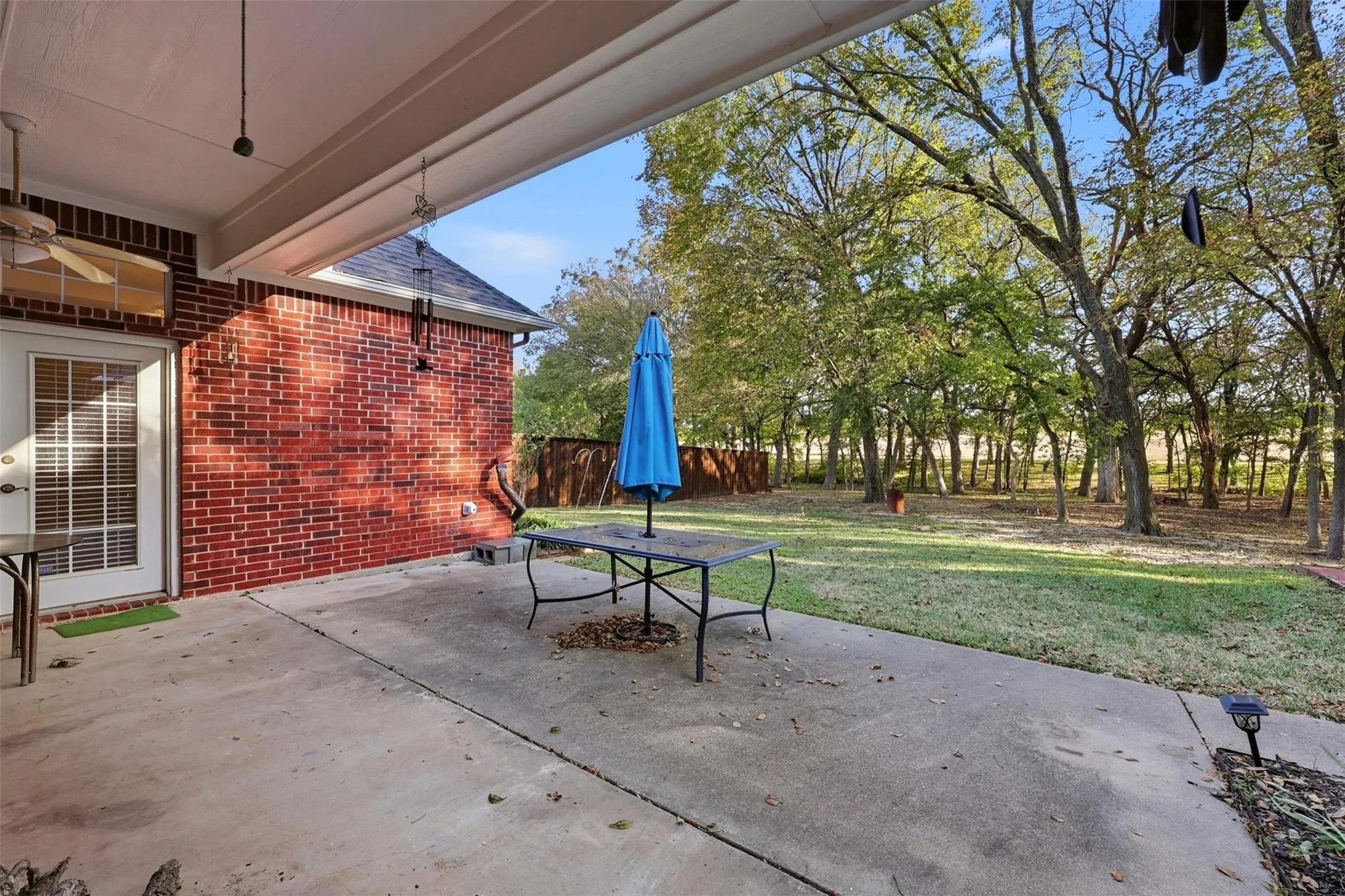 Expansive concrete patio featuring a covered area with a ceiling fan, offering direct access to a large grass yard