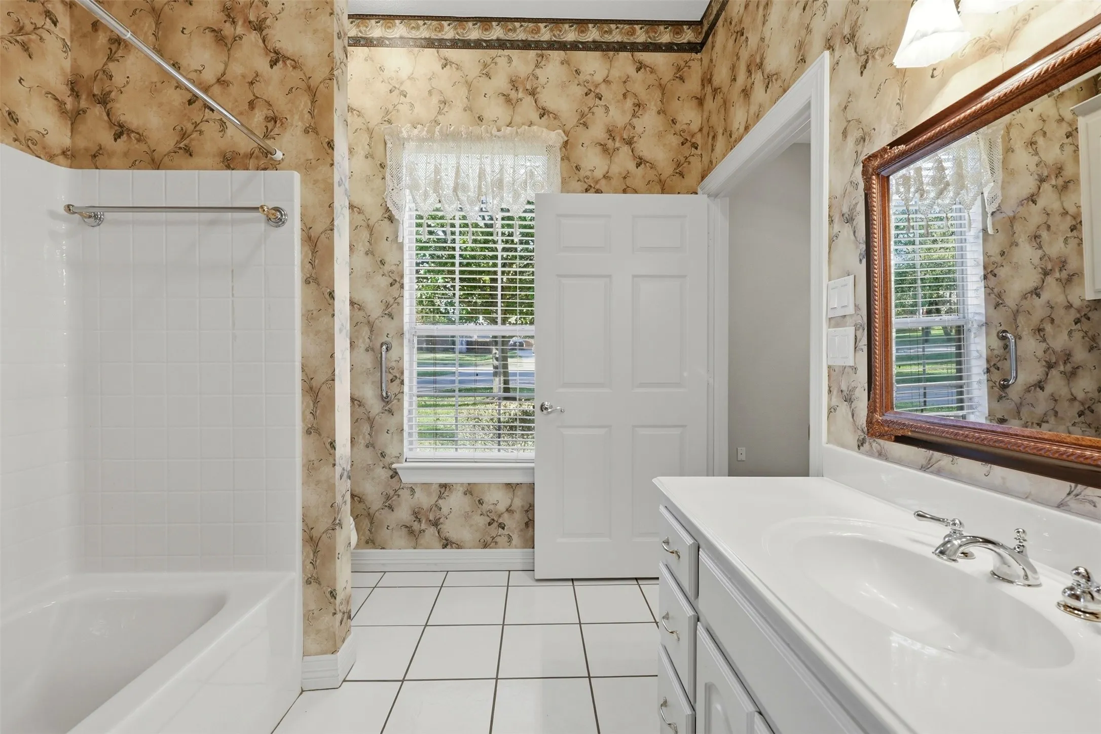 1st floor full Bathroom with wallpapered walls, light tile patterned flooring, vanity, and shower / bathtub combination