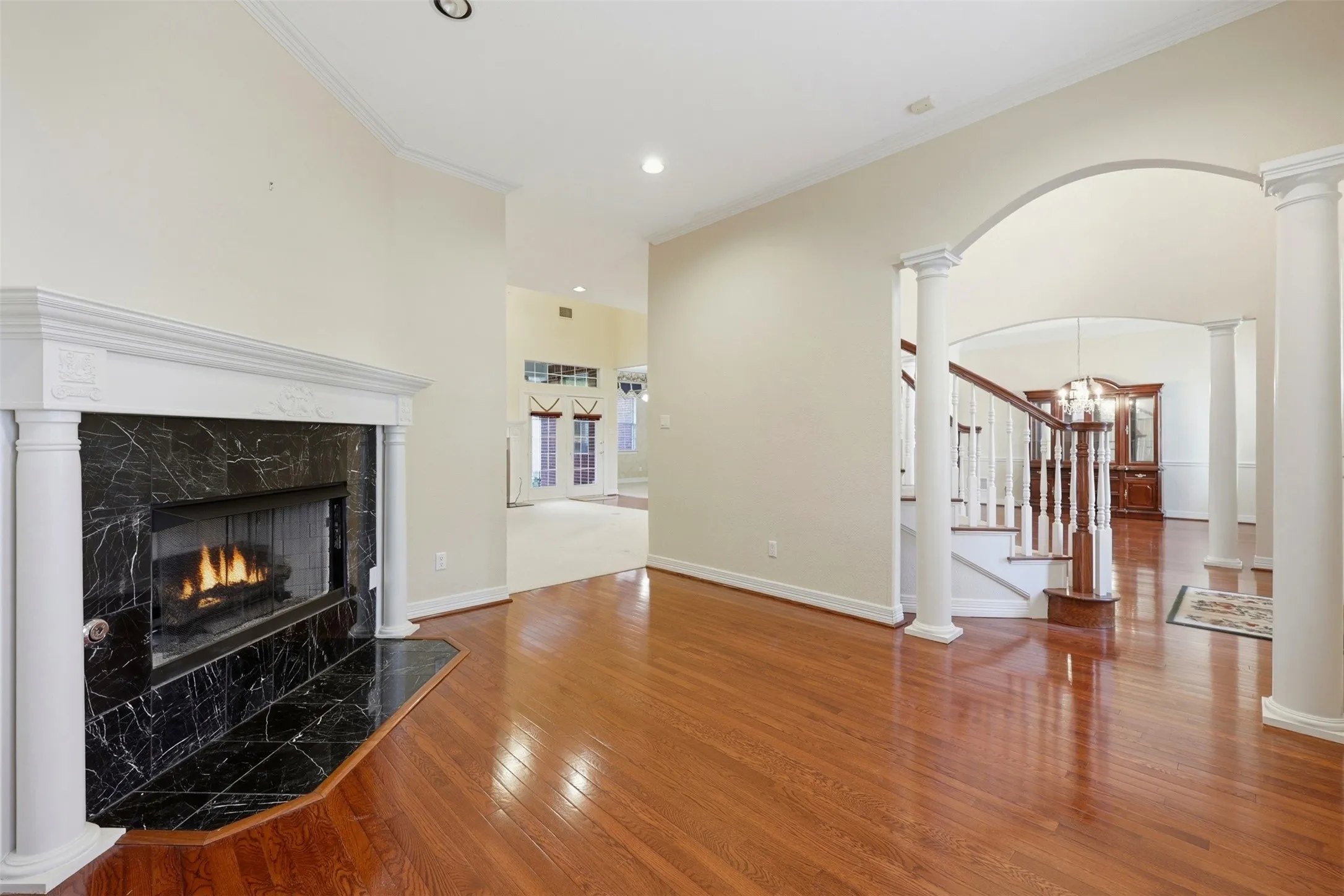 Formal living room featuring decorative columns, arched walkways, light wood-style flooring, a fireplace, and ornamental molding