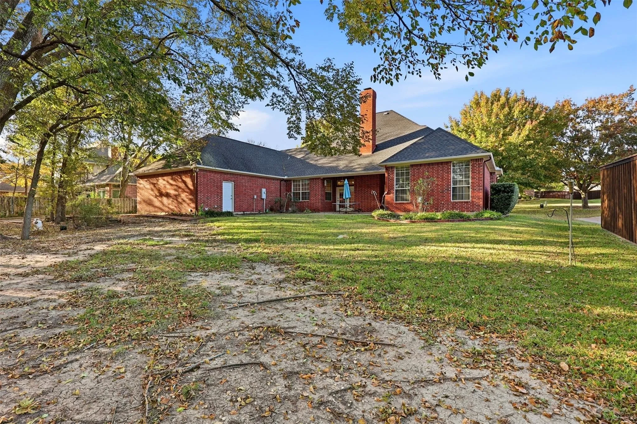 Expansive rear yard featuring a brick exterior, a covered patio, a prominent brick chimney, mature trees, and a wooden storage shed