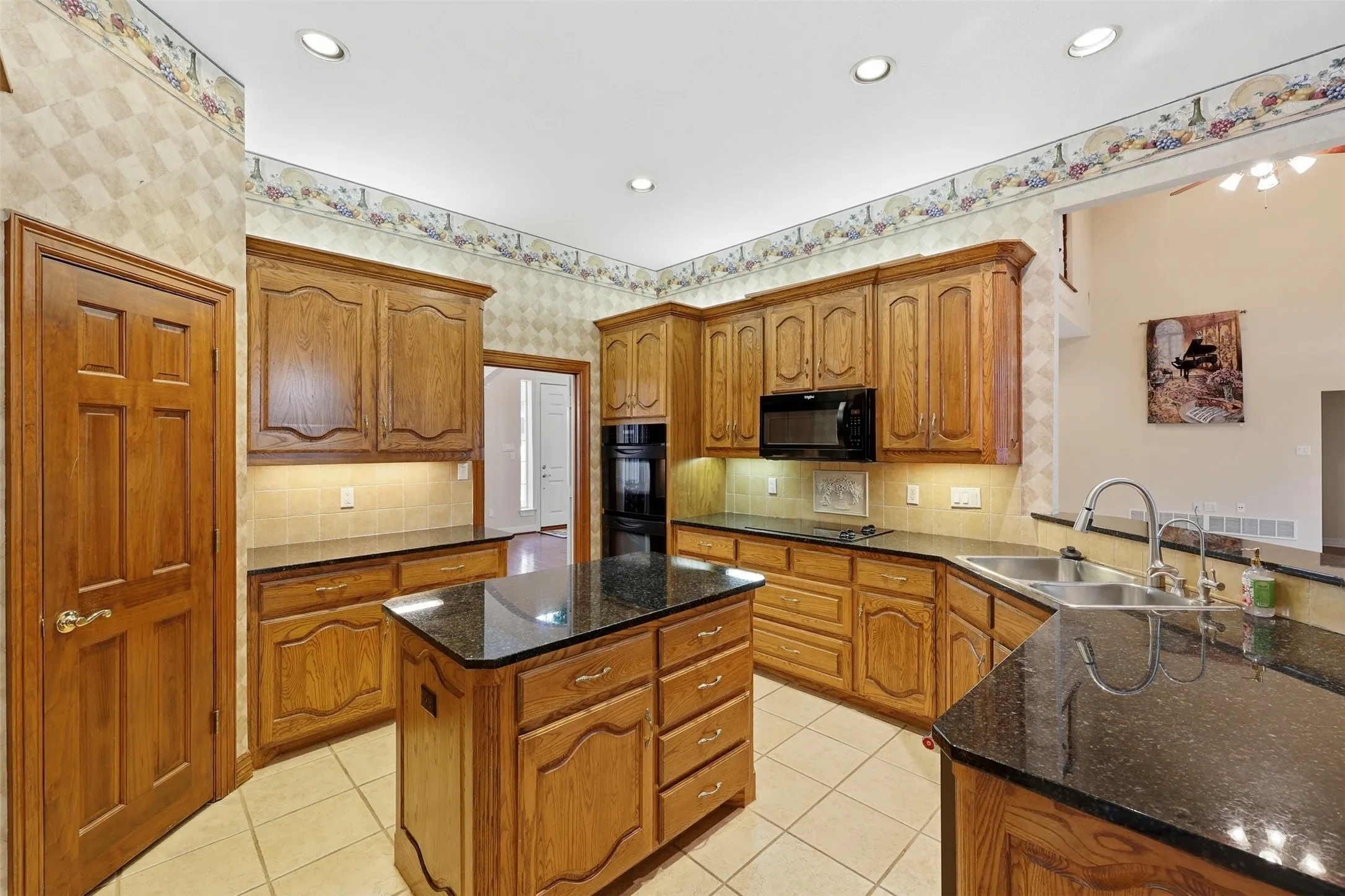 Kitchen featuring dark stone countertops, brown cabinetry, light tile patterned flooring, tasteful backsplash, and wallpapered walls