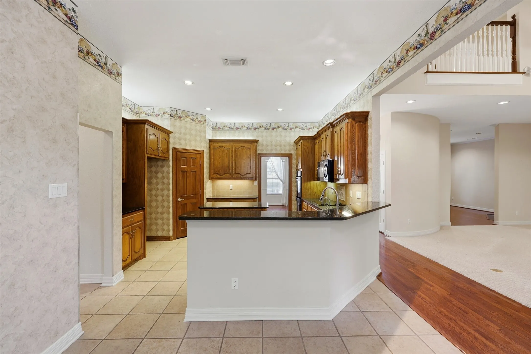 Kitchen featuring dark stone counters, recessed lighting, light tile patterned flooring, a peninsula, and brown cabinetry