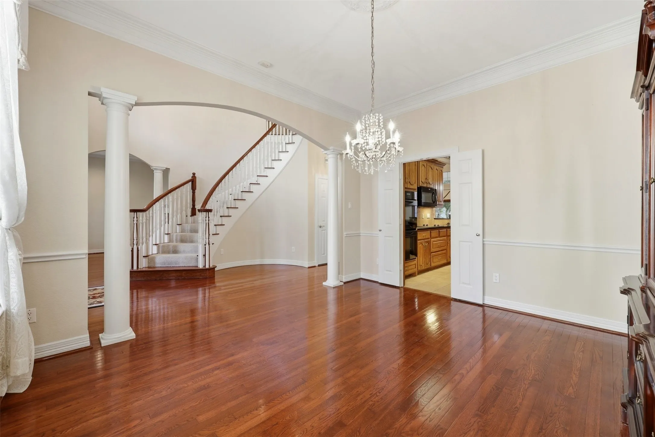Formal dining area with stairs, decorative columns, dark wood finished floors, ornamental molding, and arched walkways