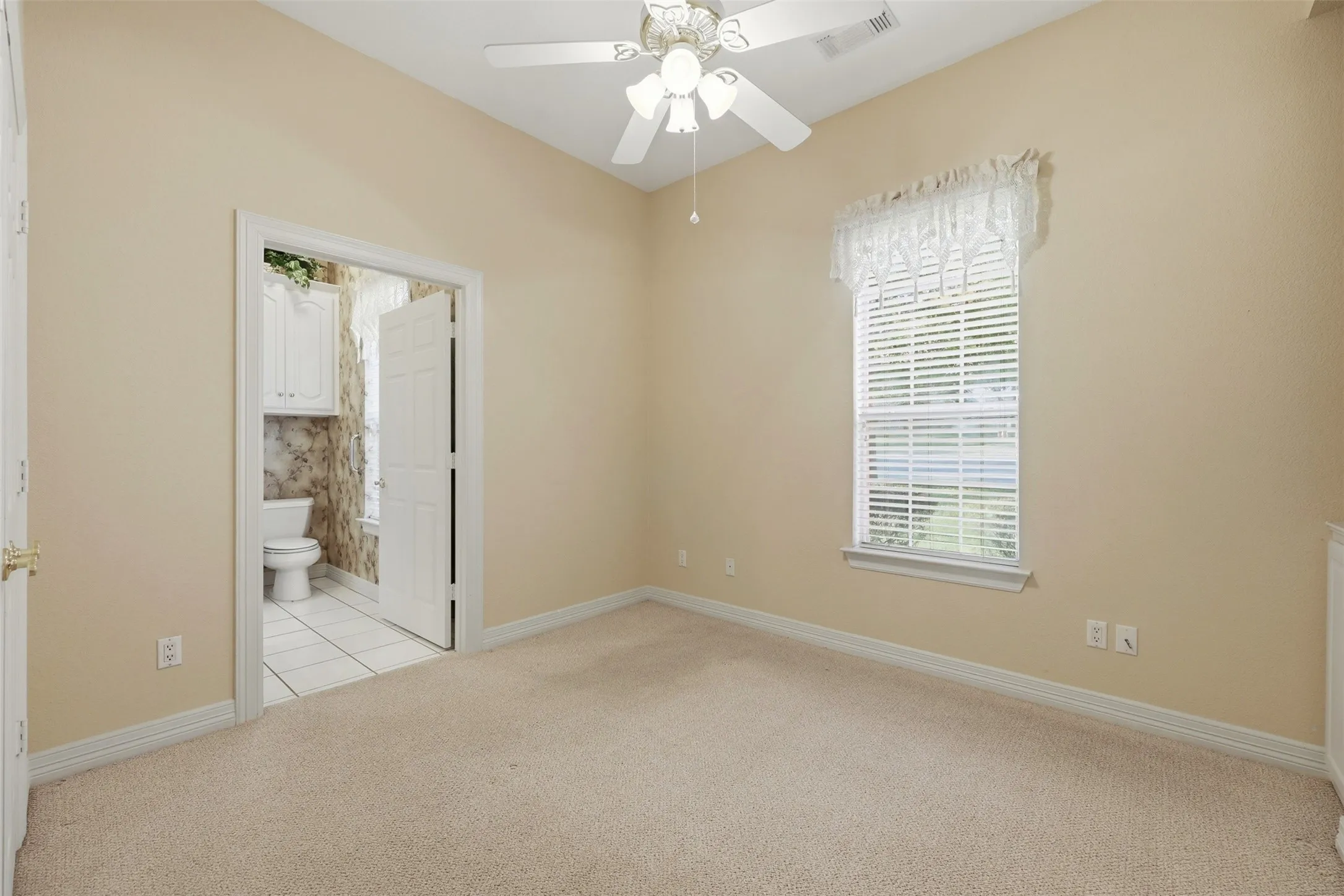 1st floor bedroom with light colored carpet, a ceiling fan, ensuite bathroom, and light tile patterned floors