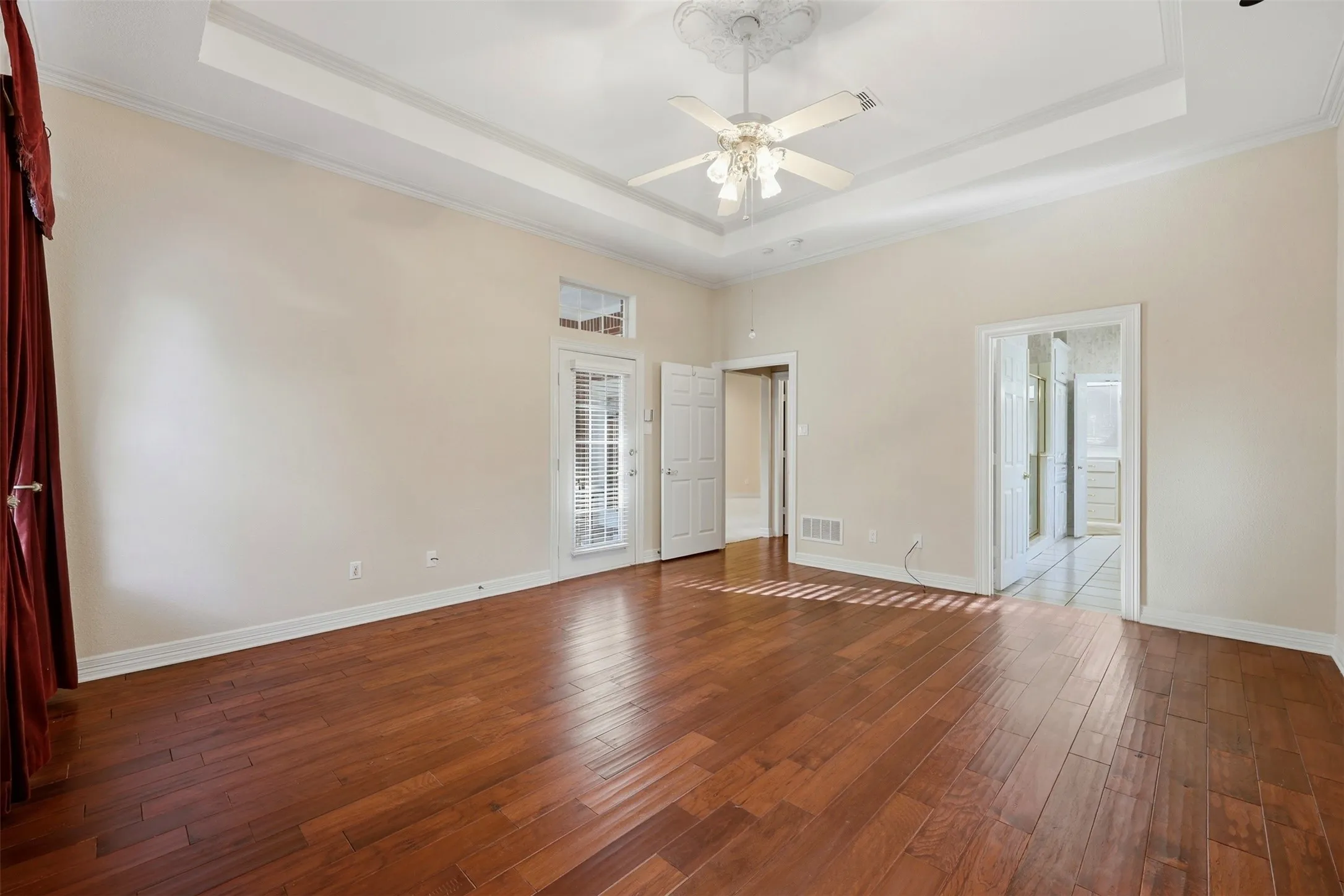 Primary bedroom with a raised ceiling, hardwood / wood-style floors, crown molding, and a ceiling fan