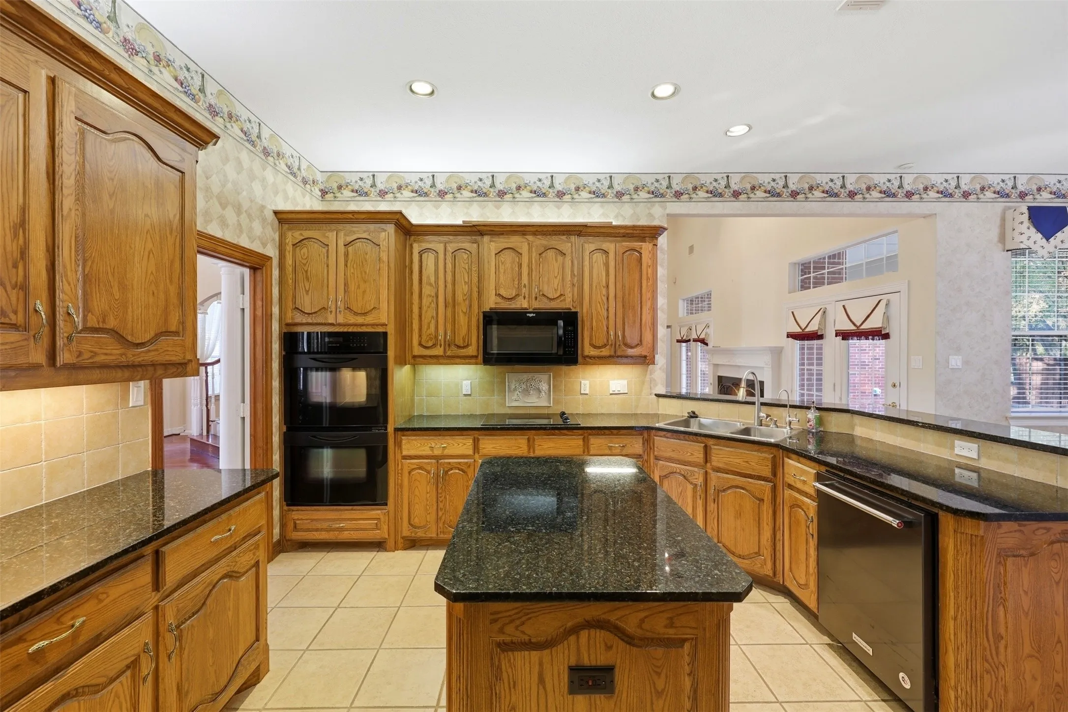Kitchen featuring light tile patterned floors, brown cabinets, dark stone counters, wallpapered walls, and recessed lighting