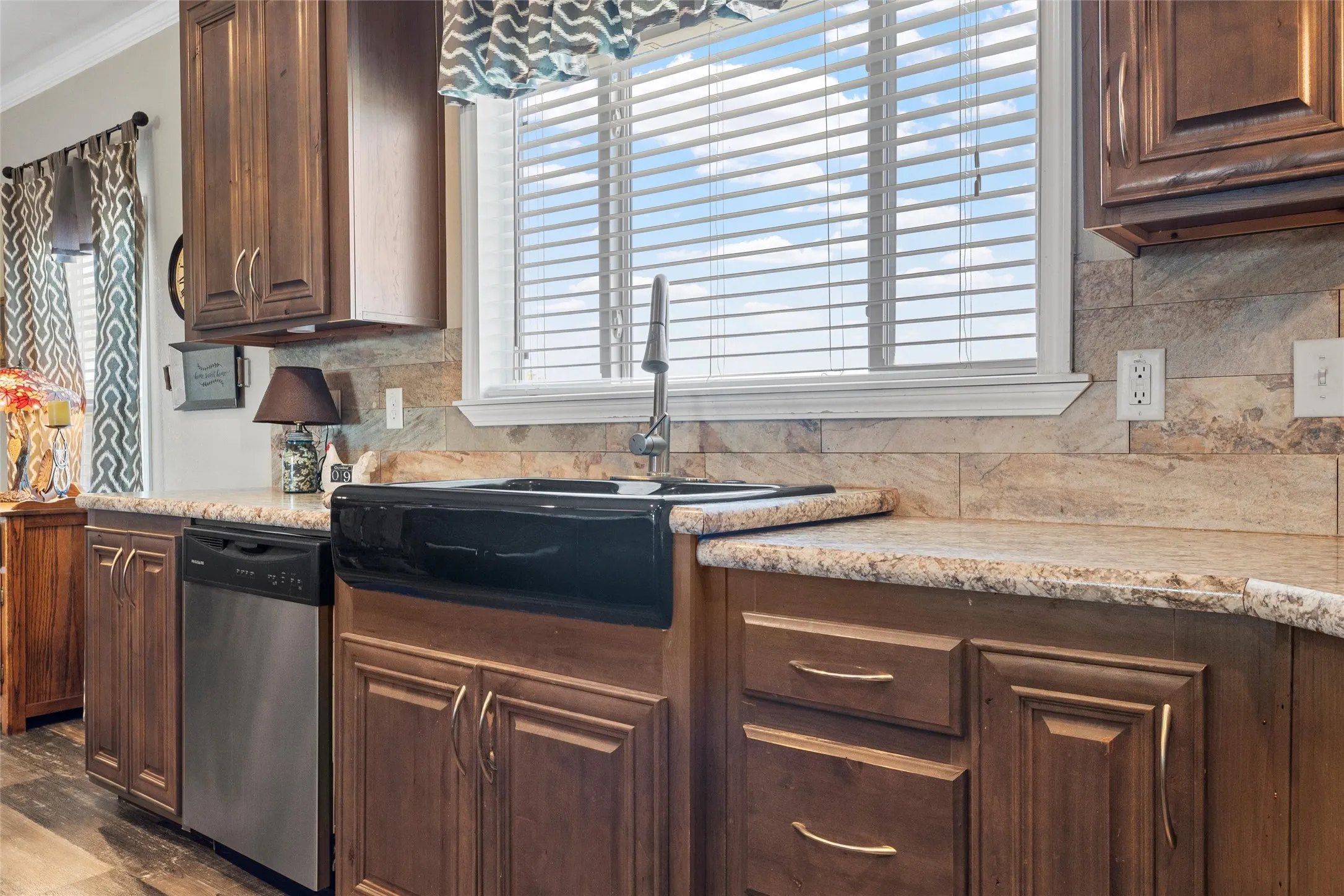 Kitchen with dark brown cabinets, decorative backsplash, dishwasher, crown molding, and light stone counters