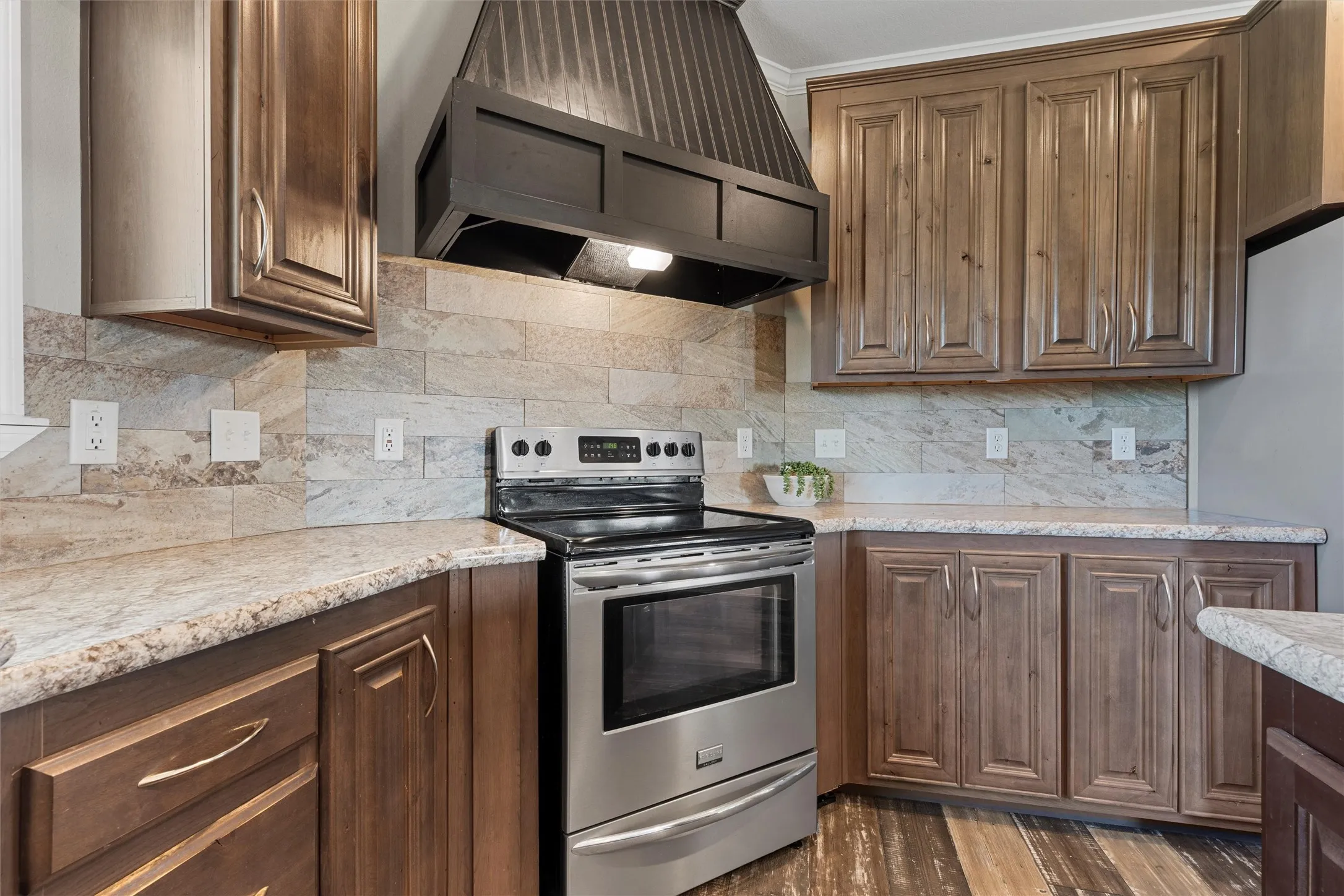 Kitchen with stainless steel appliances, premium range hood, tasteful backsplash, dark wood-type flooring, and light stone counters