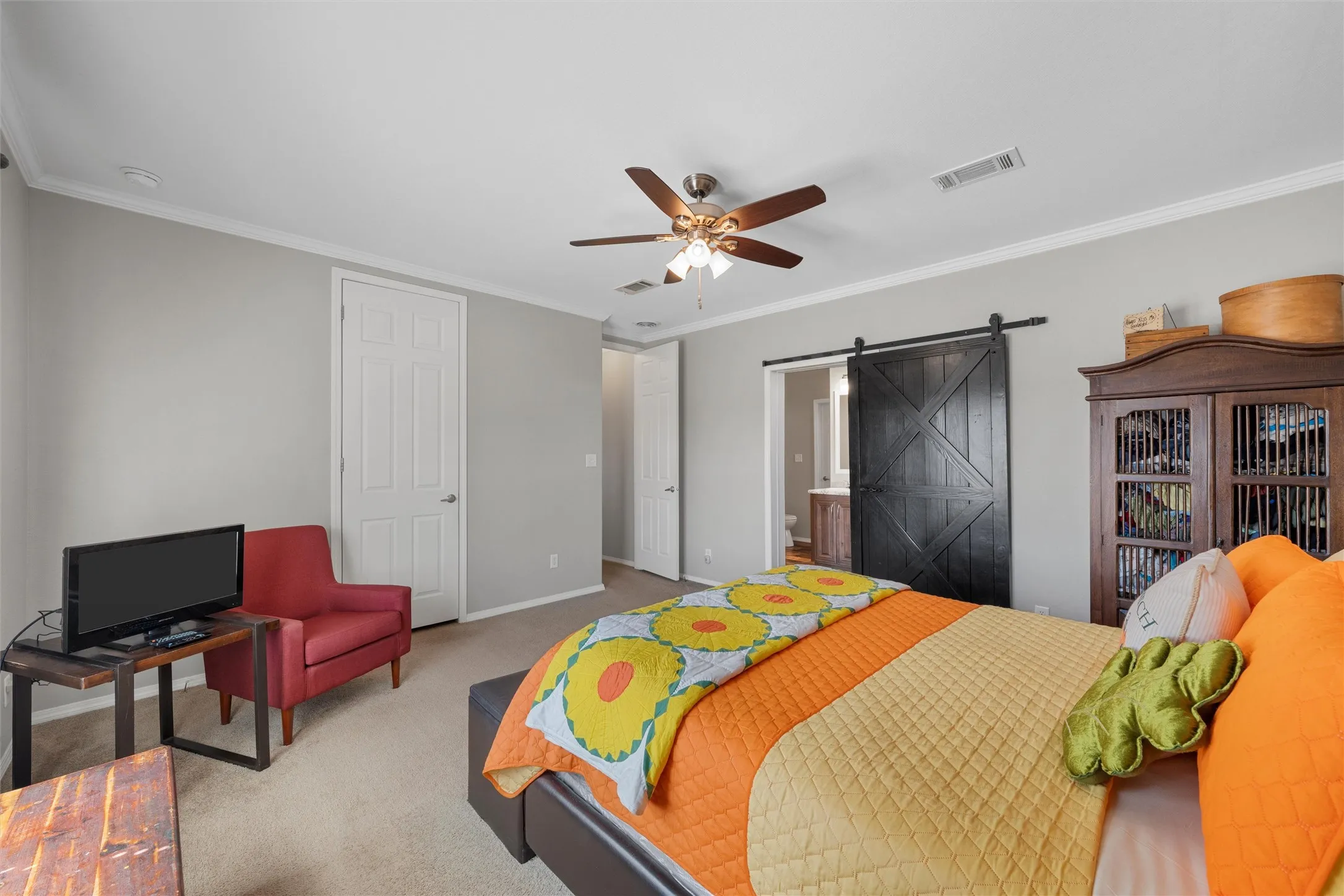 Carpeted bedroom featuring a barn door, crown molding, a ceiling fan, a closet, and ensuite bath