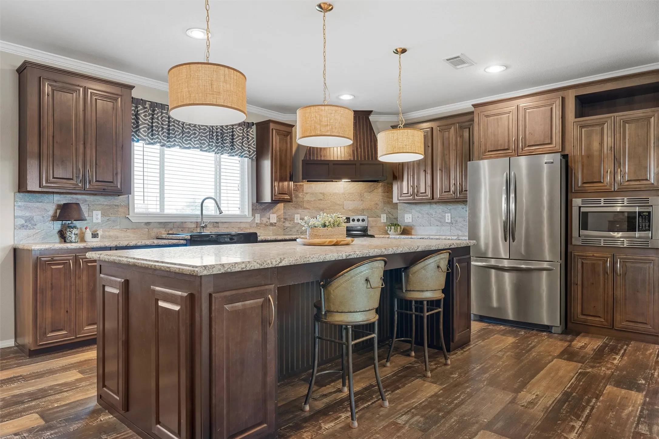 Kitchen with appliances with stainless steel finishes, ornamental molding, dark wood-style flooring, a kitchen island, and tasteful backsplash