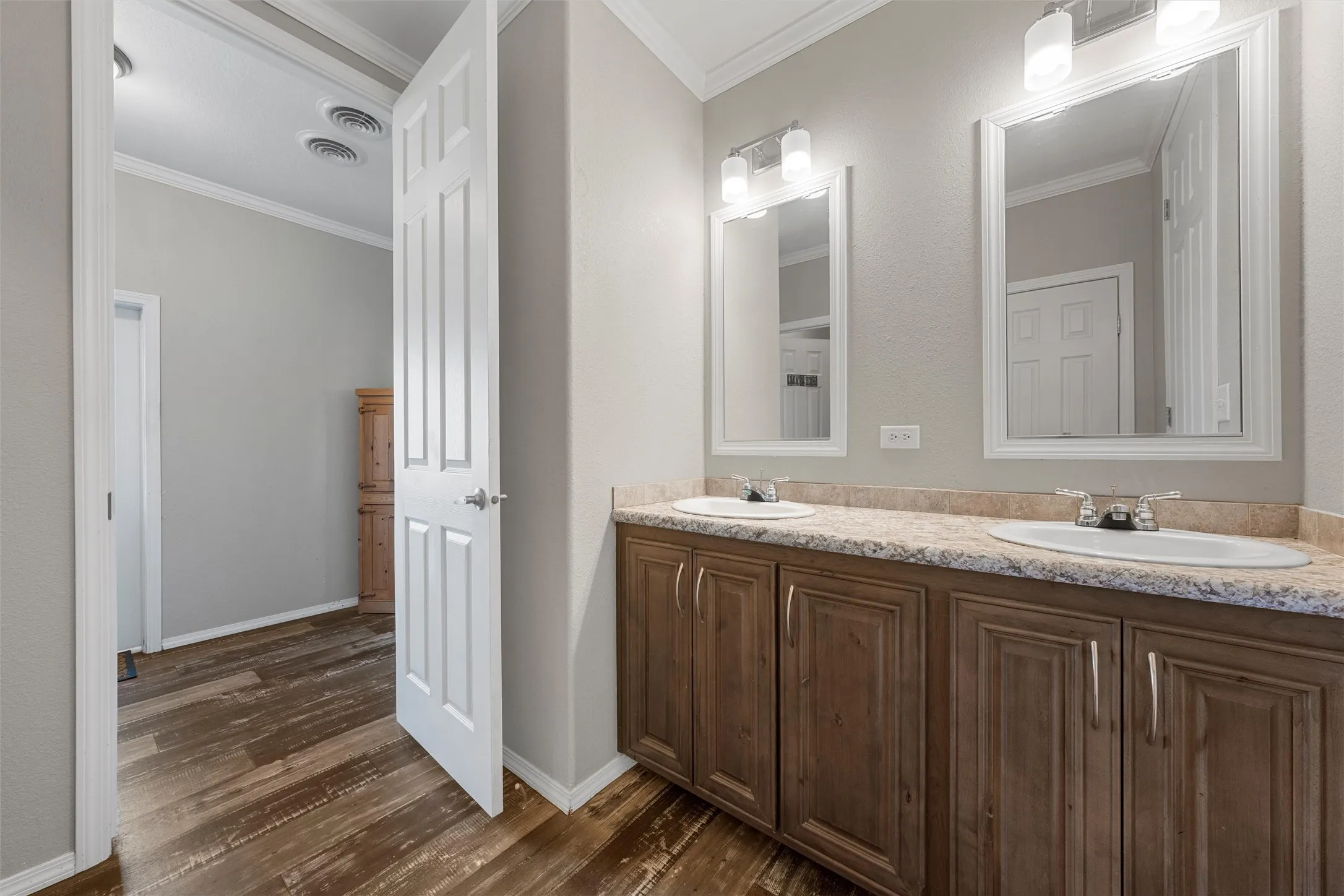 Bathroom with ornamental molding, double vanity, and dark wood-style floors