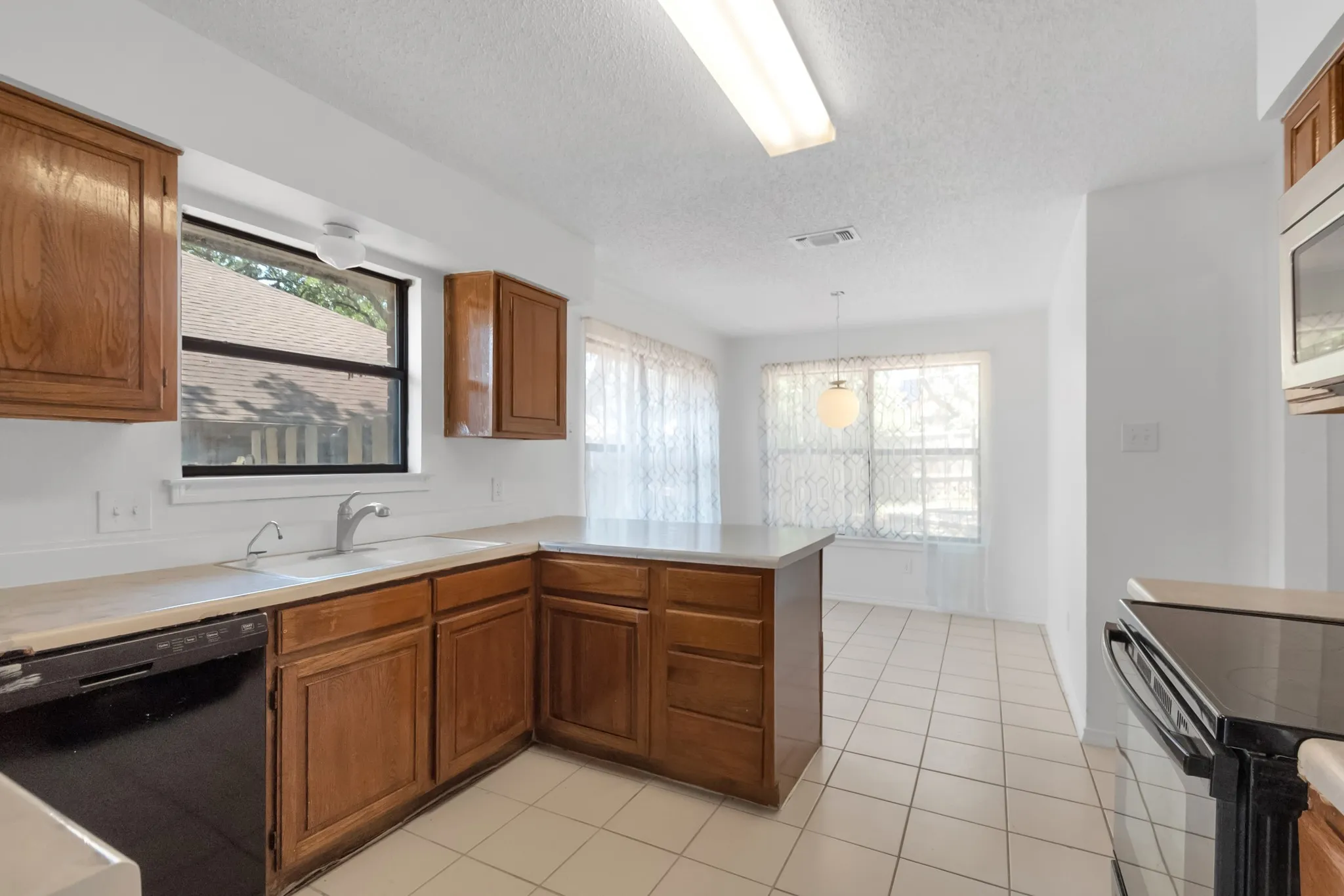 Spacious kitchen featuring wood-finish cabinetry, ceramic tile flooring, and stainless steel appliances including a built-in wall oven and range