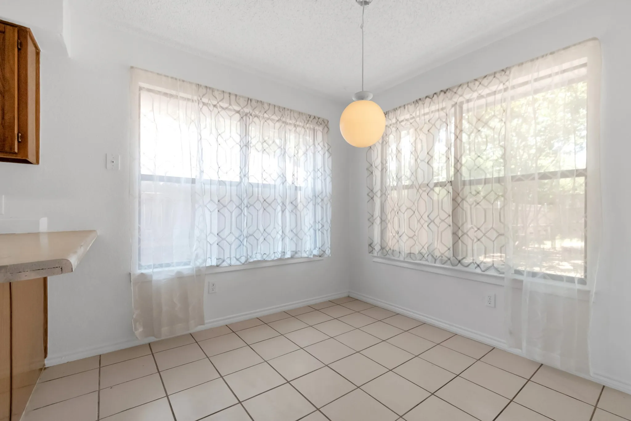 Bright corner dining area bathed in natural light from dual windows with geometric patterned sheers