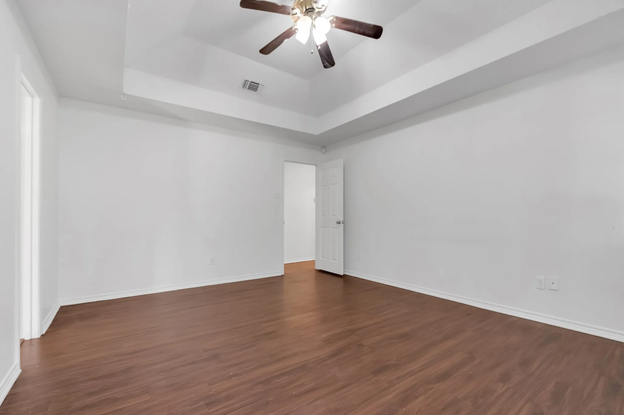 Spacious room featuring warm wood-finish flooring, clean white walls, and a coffered ceiling with ceiling fan and integrated lighting