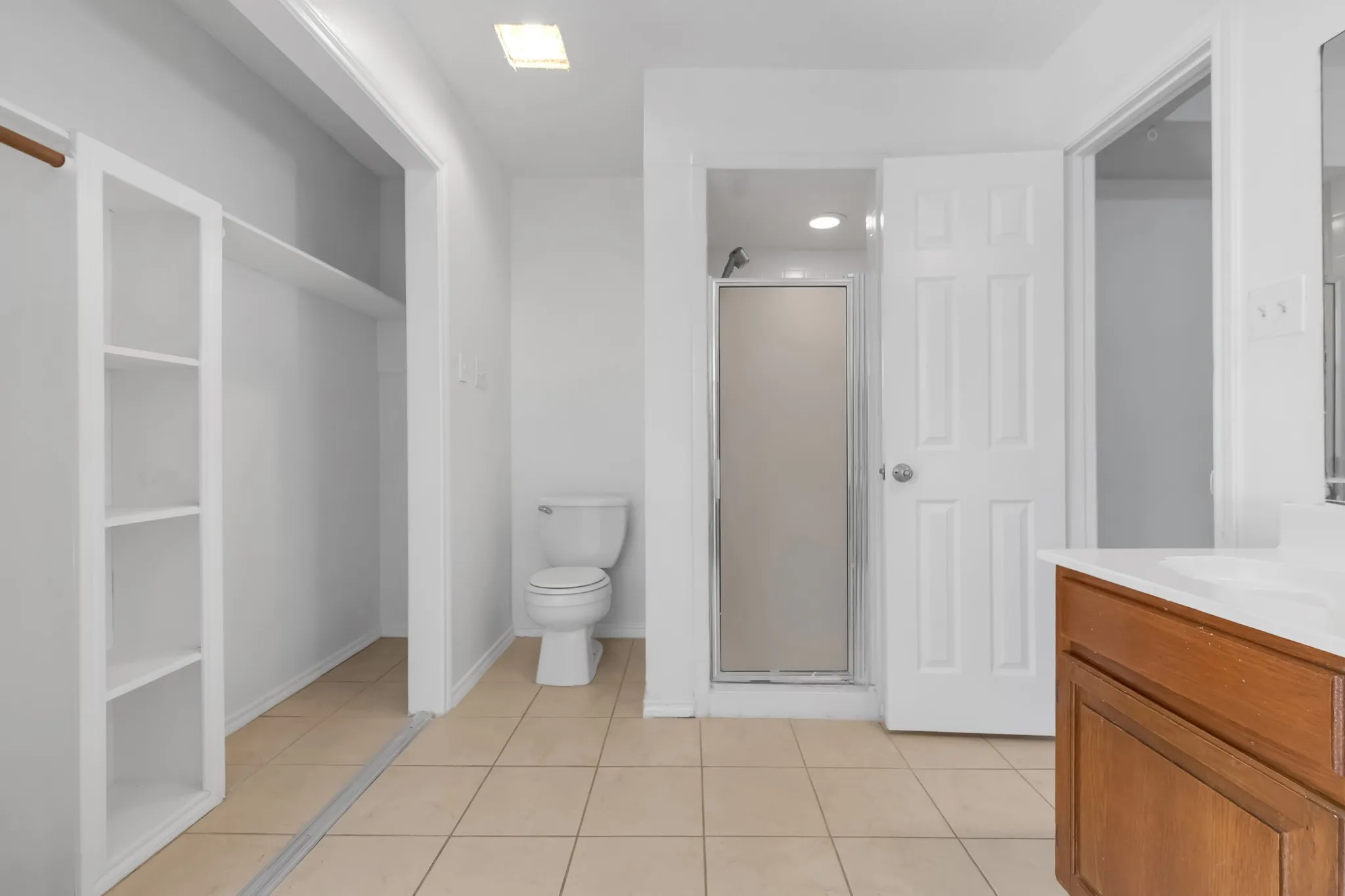 Bathroom featuring a built-in wood-finish vanity with a single sink, an enclosed shower, a toilet, a built-in closet with shelving, and tile flooring