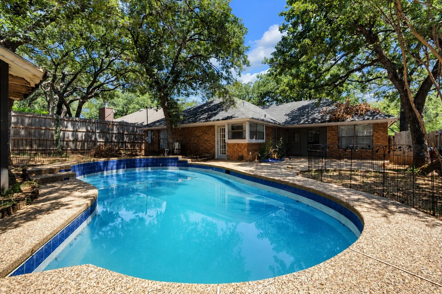 Kidney-shaped swimming pool featuring blue and white tile accents and a textured aggregate deck