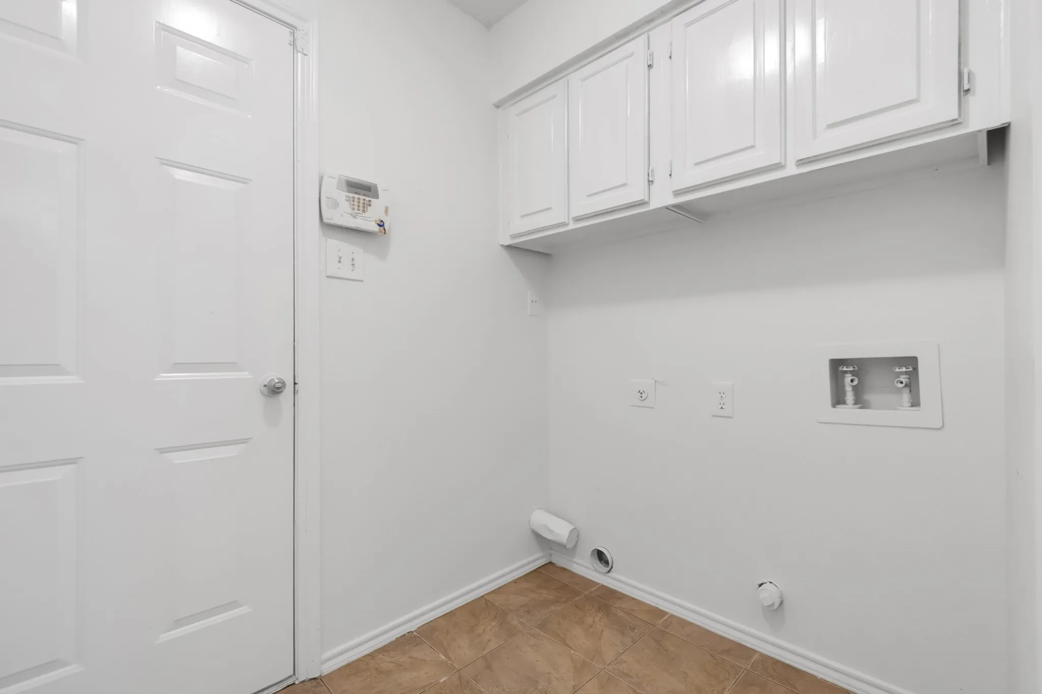 Dedicated utility space featuring overhead white cabinetry, tile flooring, and appliance hookups