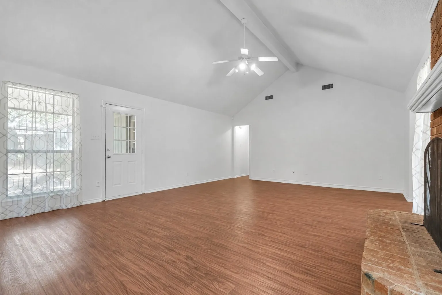 Spacious open room featuring gleaming wood-finish flooring, vaulted ceiling with ceiling fan, and abundant natural light from multiple windows and glass doors