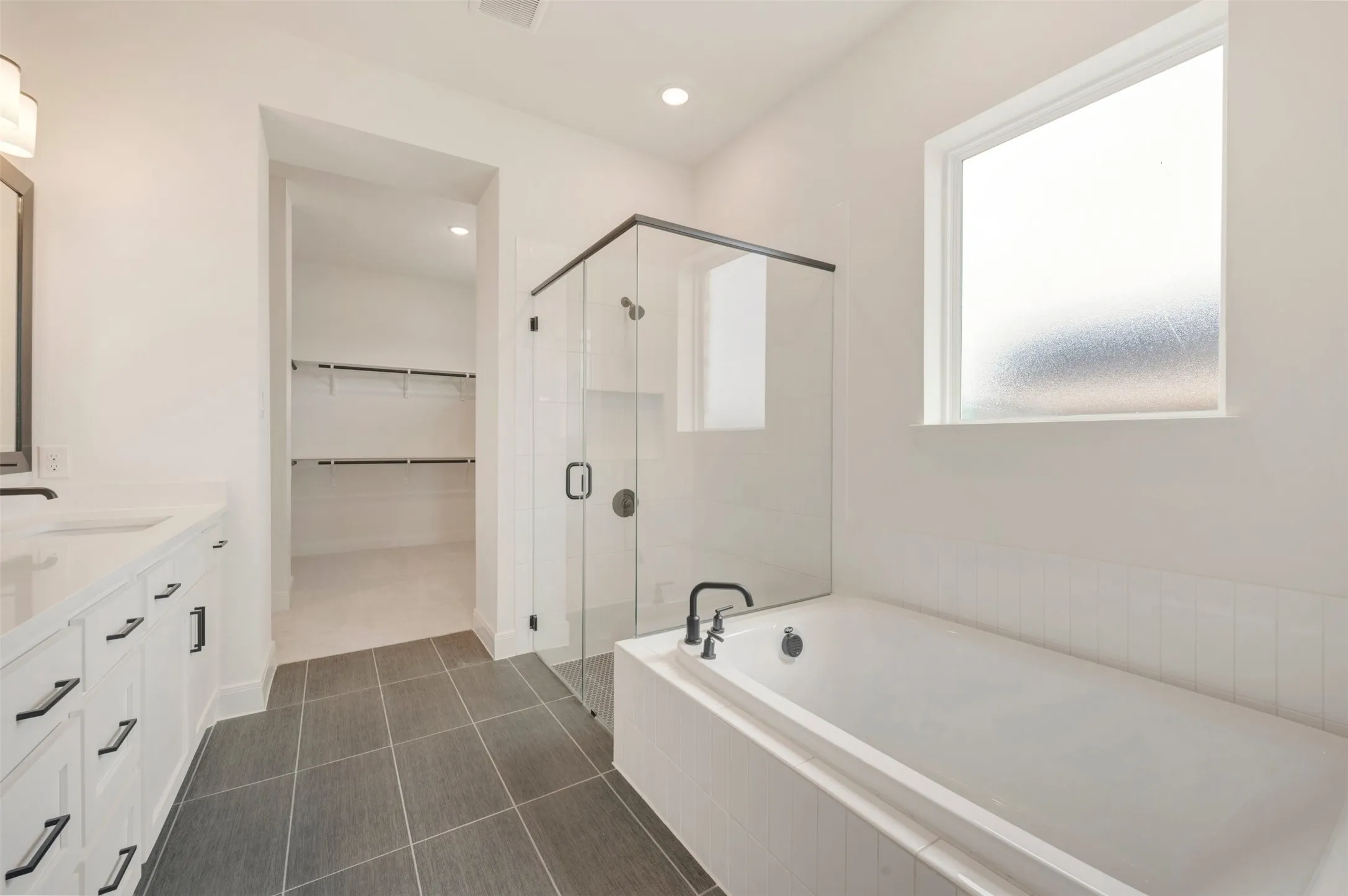 Modern bath featuring a frameless glass shower enclosure, a built-in soaking tub, and a vanity with dual sinks