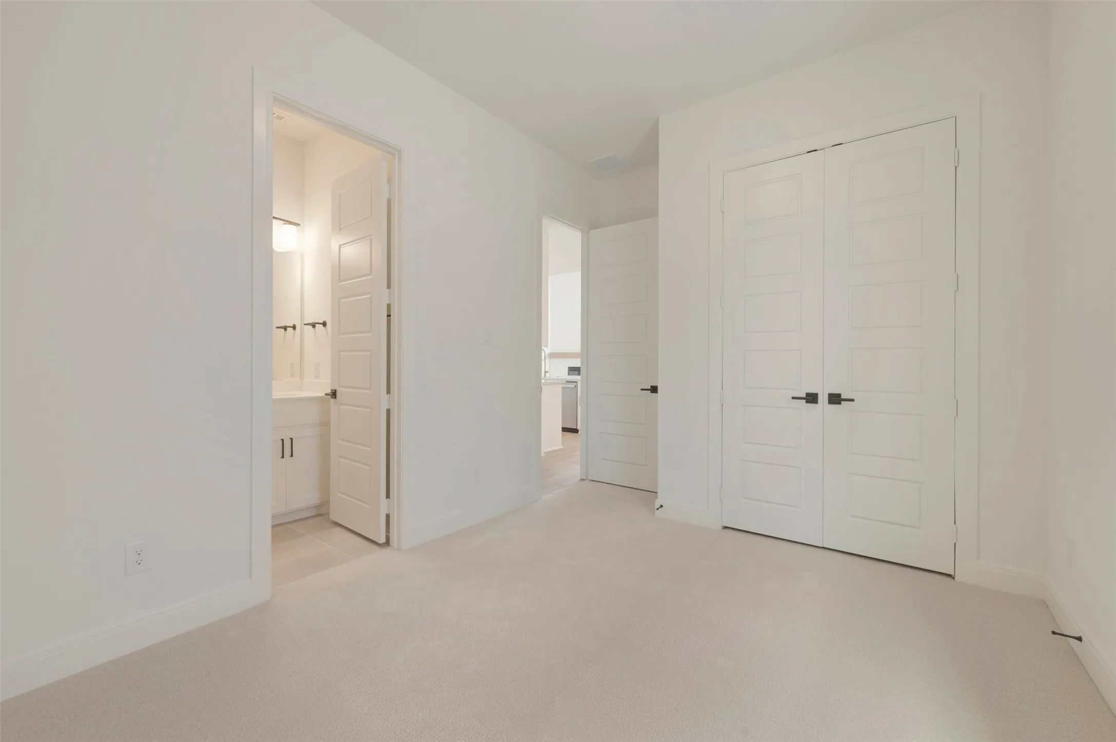 Carpeted room featuring white walls, white baseboards, and a double-door closet with matte black hardware