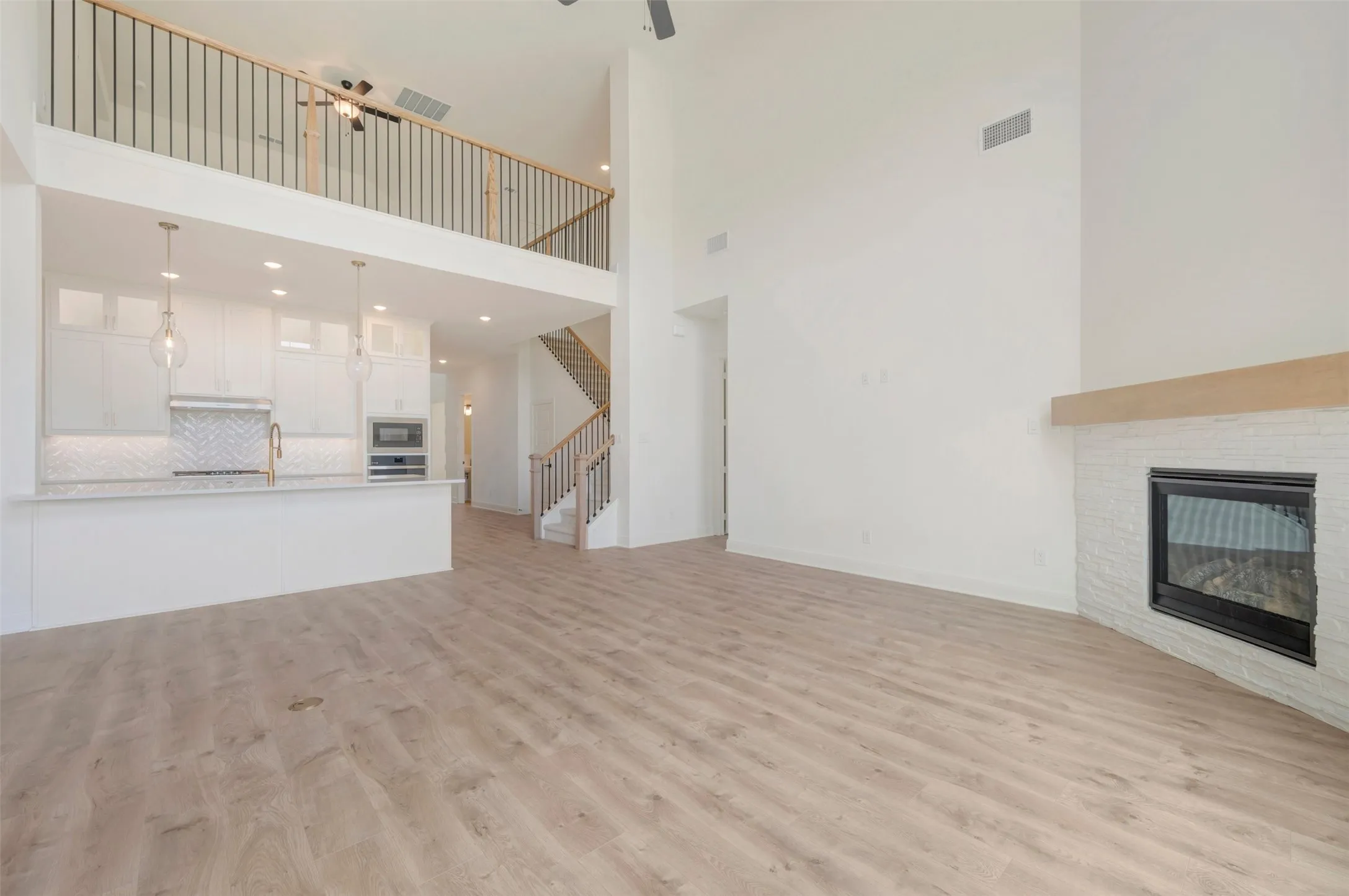 Spacious living area featuring wood-finish flooring, a white brick fireplace with a wood mantle, and high ceilings